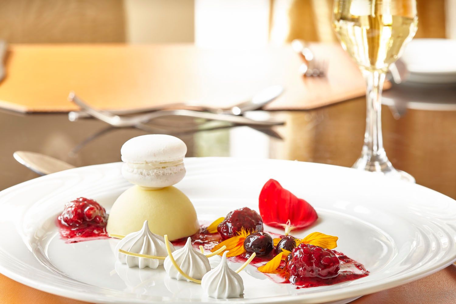 Prato branco com sobremesa: macaron, creme, frutas vermelhas, merengue, frutas cítricas e champanhe.