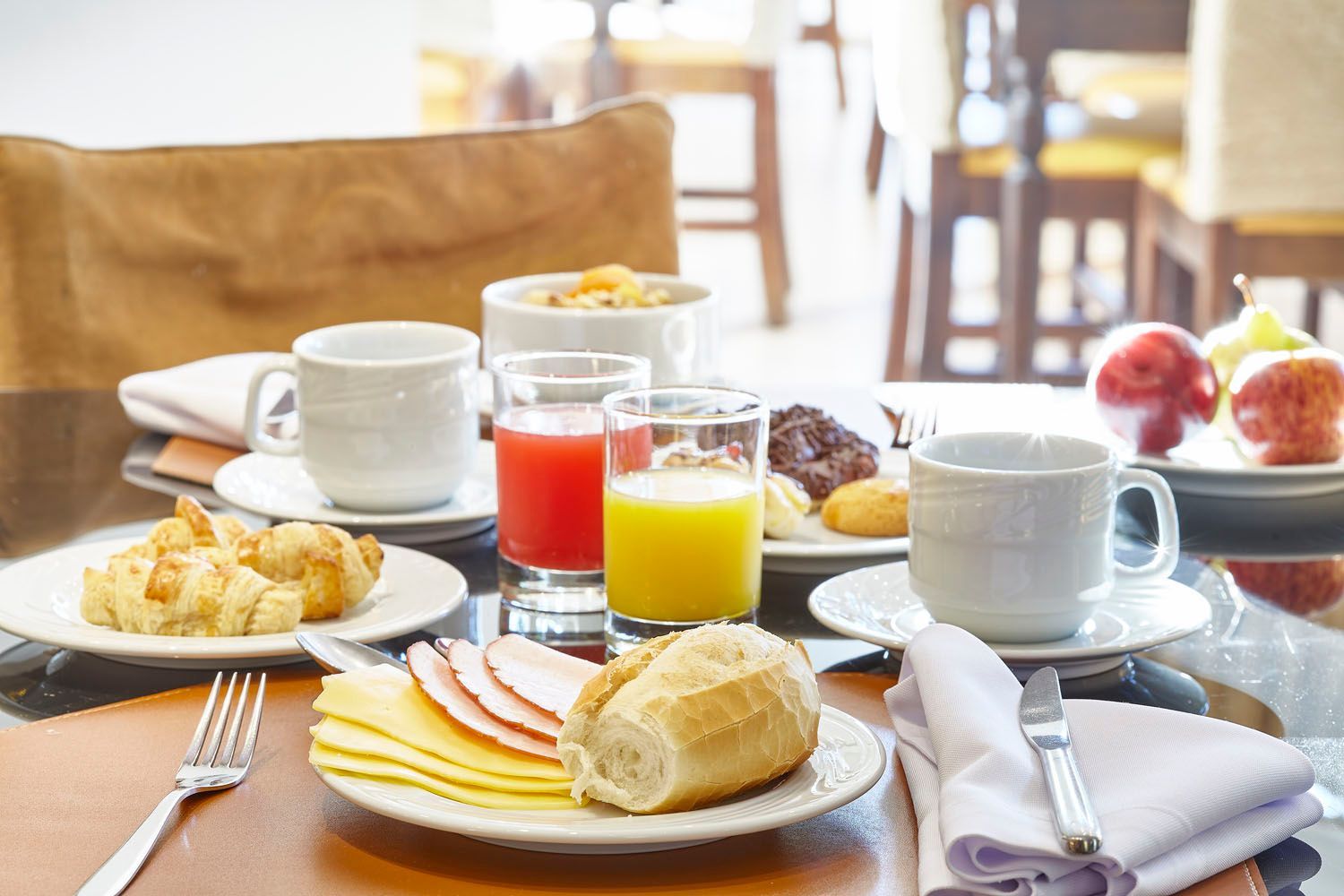 Café da manhã: croissants, suco, frutas, café, pão, presunto e queijo em uma mesa na sala de jantar.