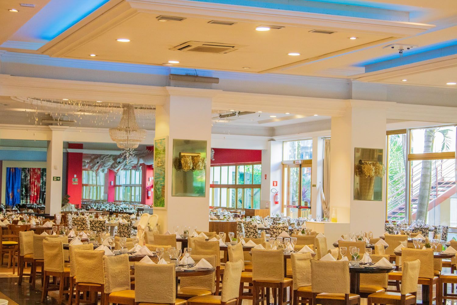 Sala de jantar bem iluminada com fileiras de mesas preparadas para uma refeição.