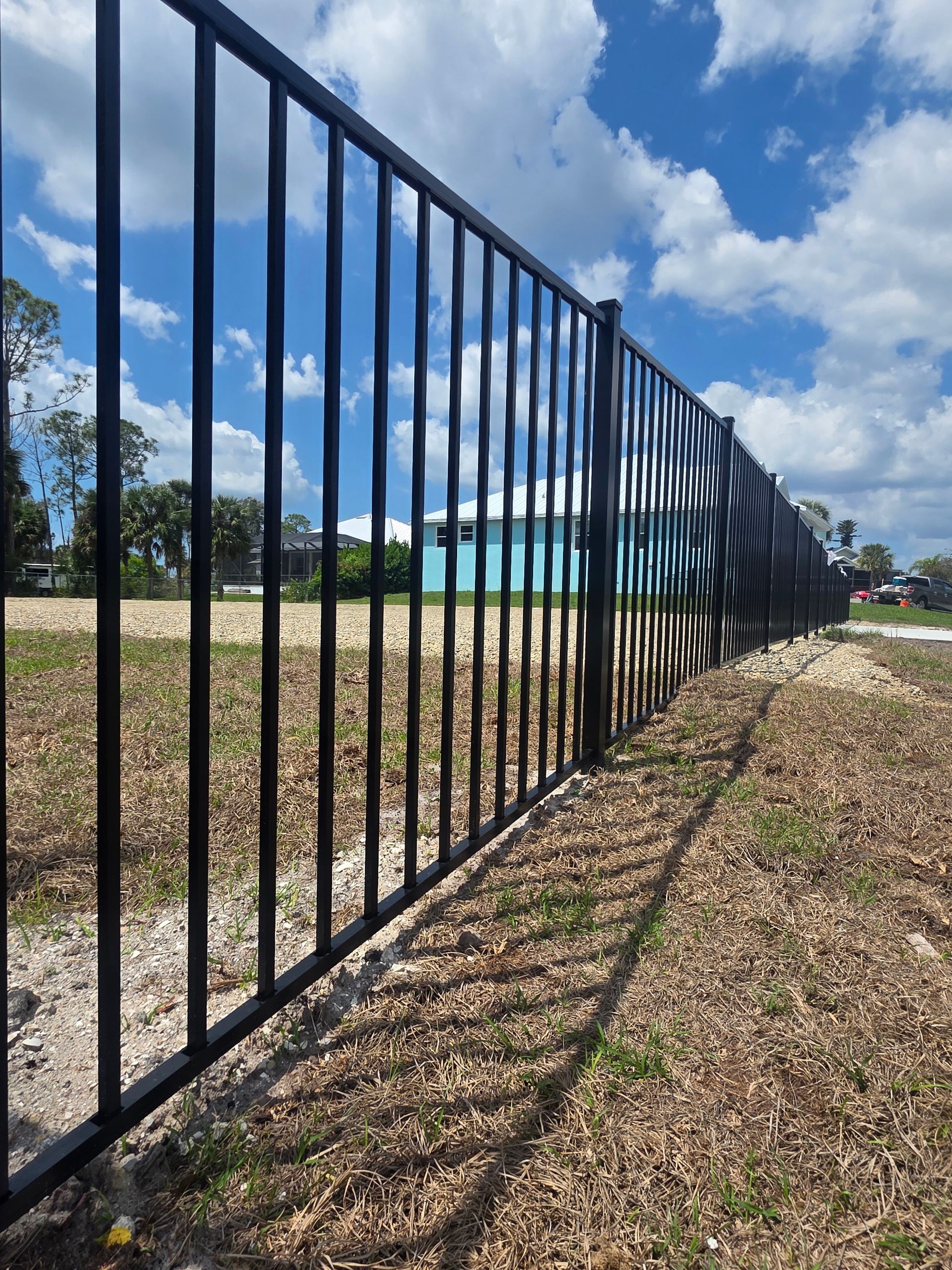 Black metal fence beside a grassy yard under a blue sky with clouds