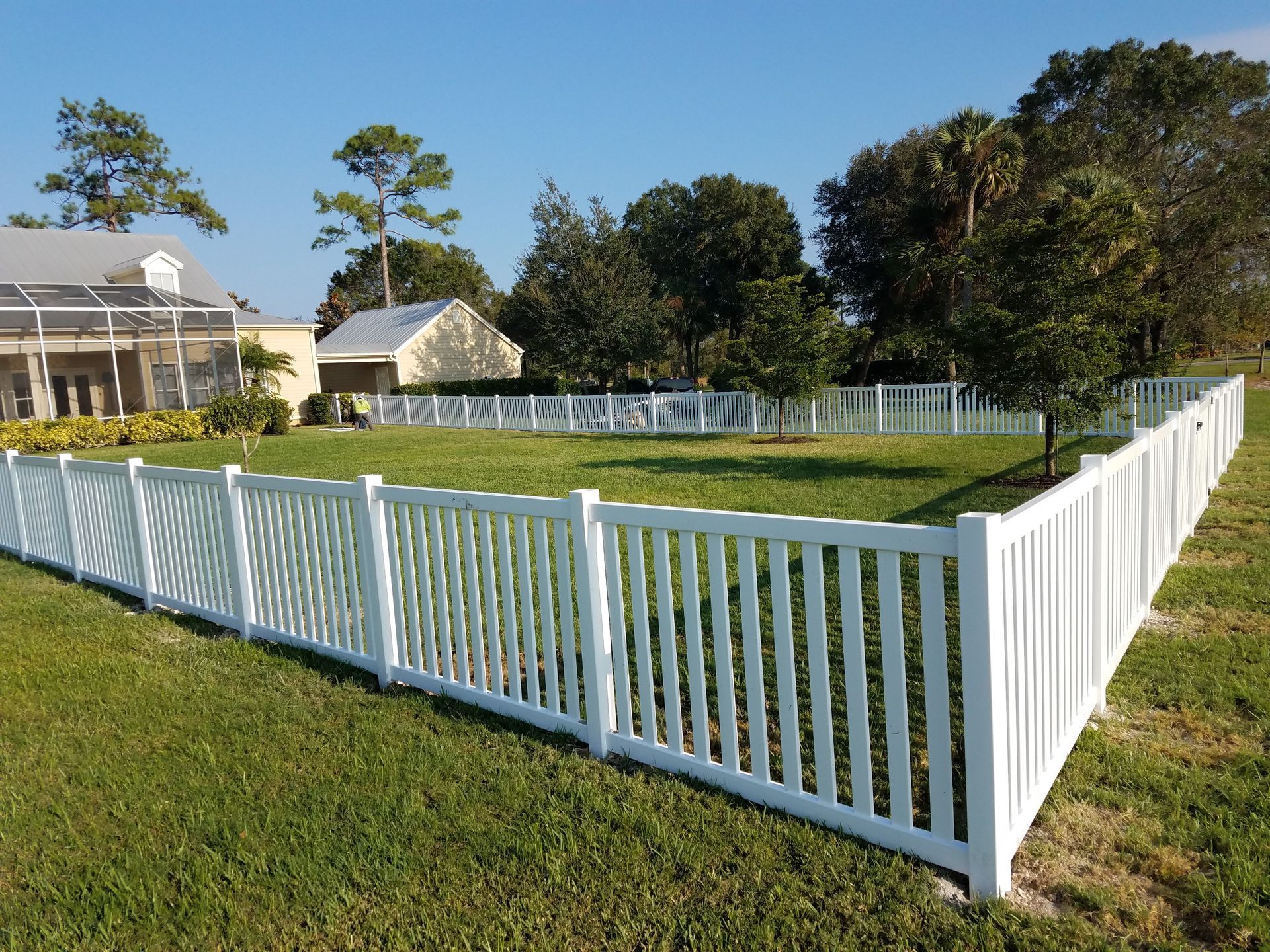 A white fence surrounds a lush green field in front of a house.