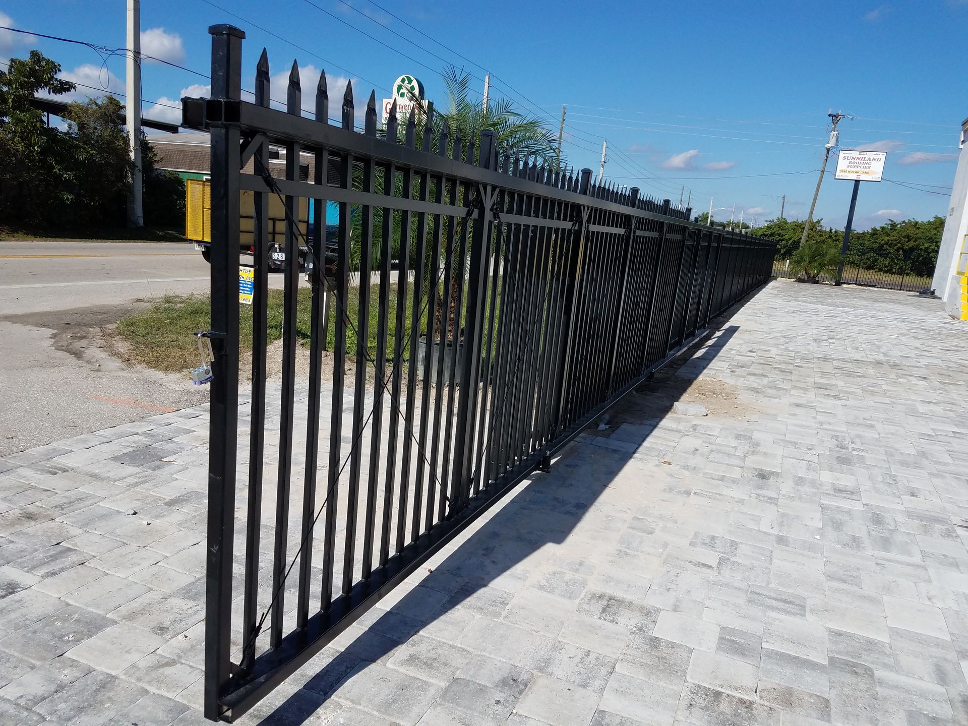 A black metal fence is sitting on top of a brick driveway.