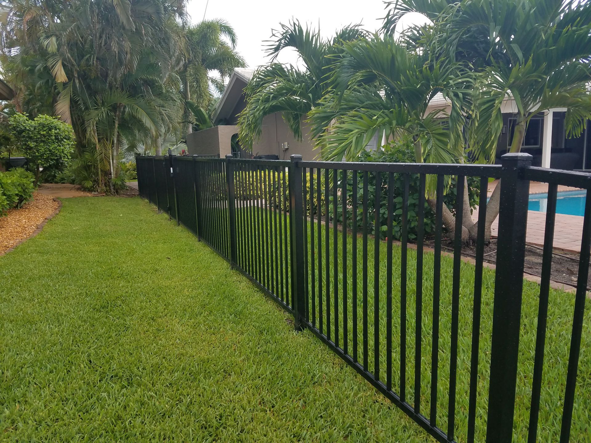 A black fence surrounds a lush green lawn in front of a house.