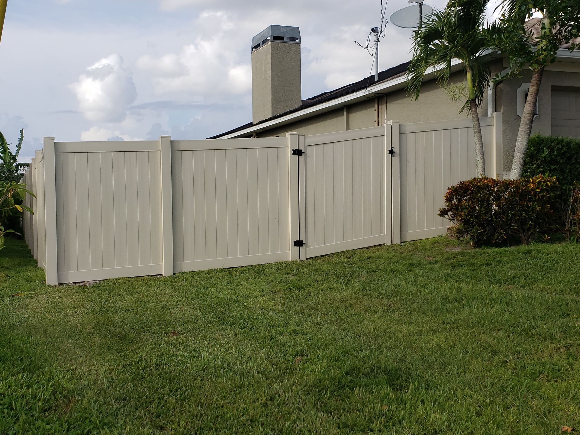 A white fence surrounds a lush green yard in front of a house.