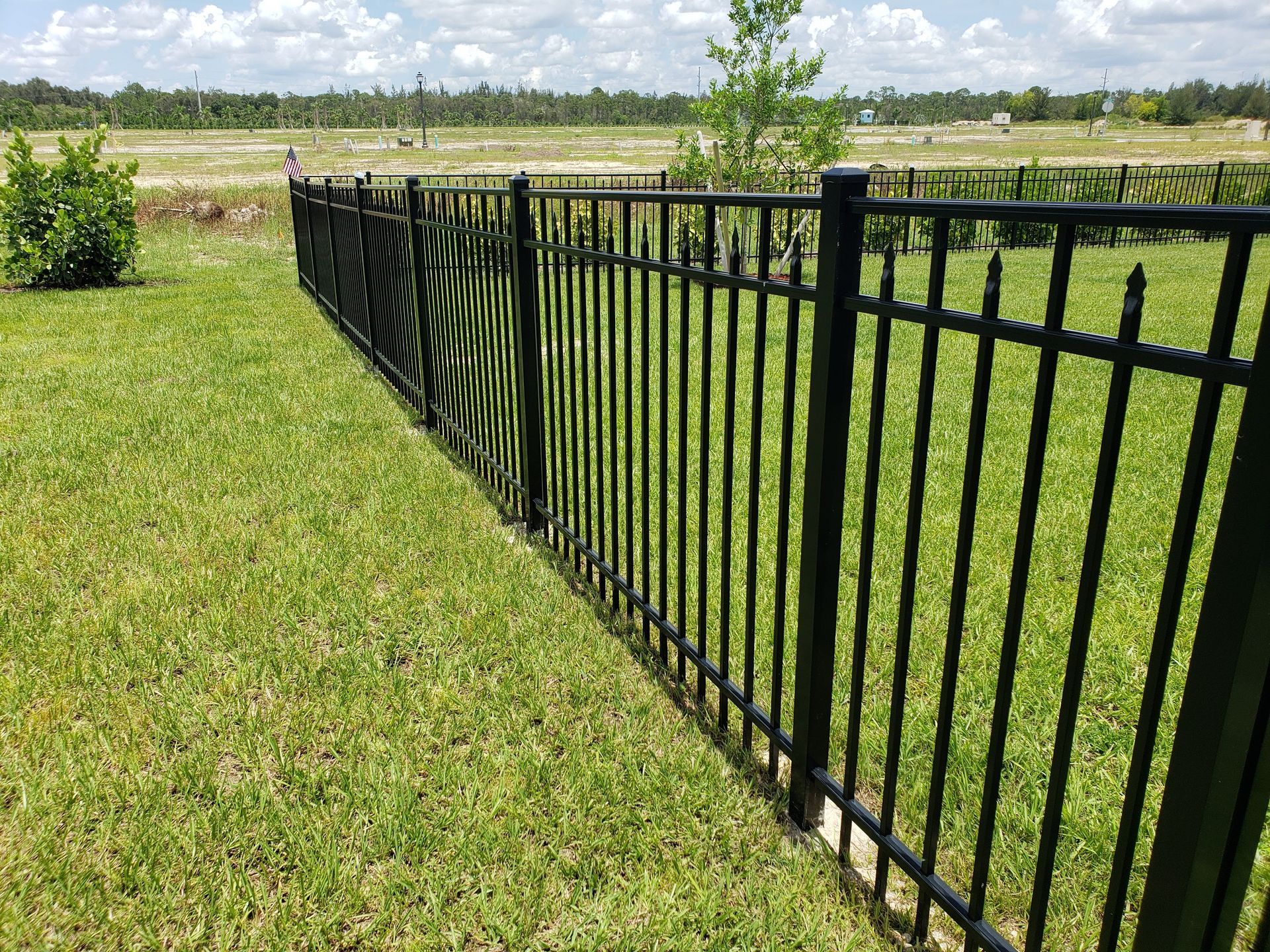 A black metal fence surrounds a lush green field.