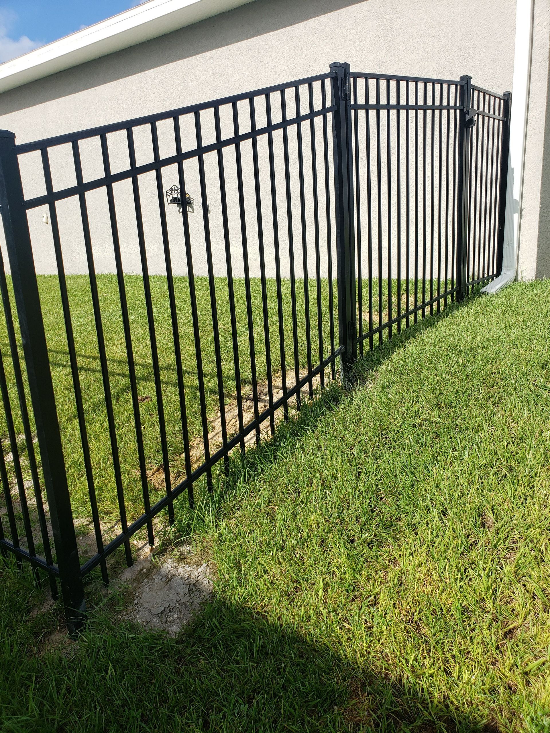 A black metal fence is sitting in the grass in front of a house.