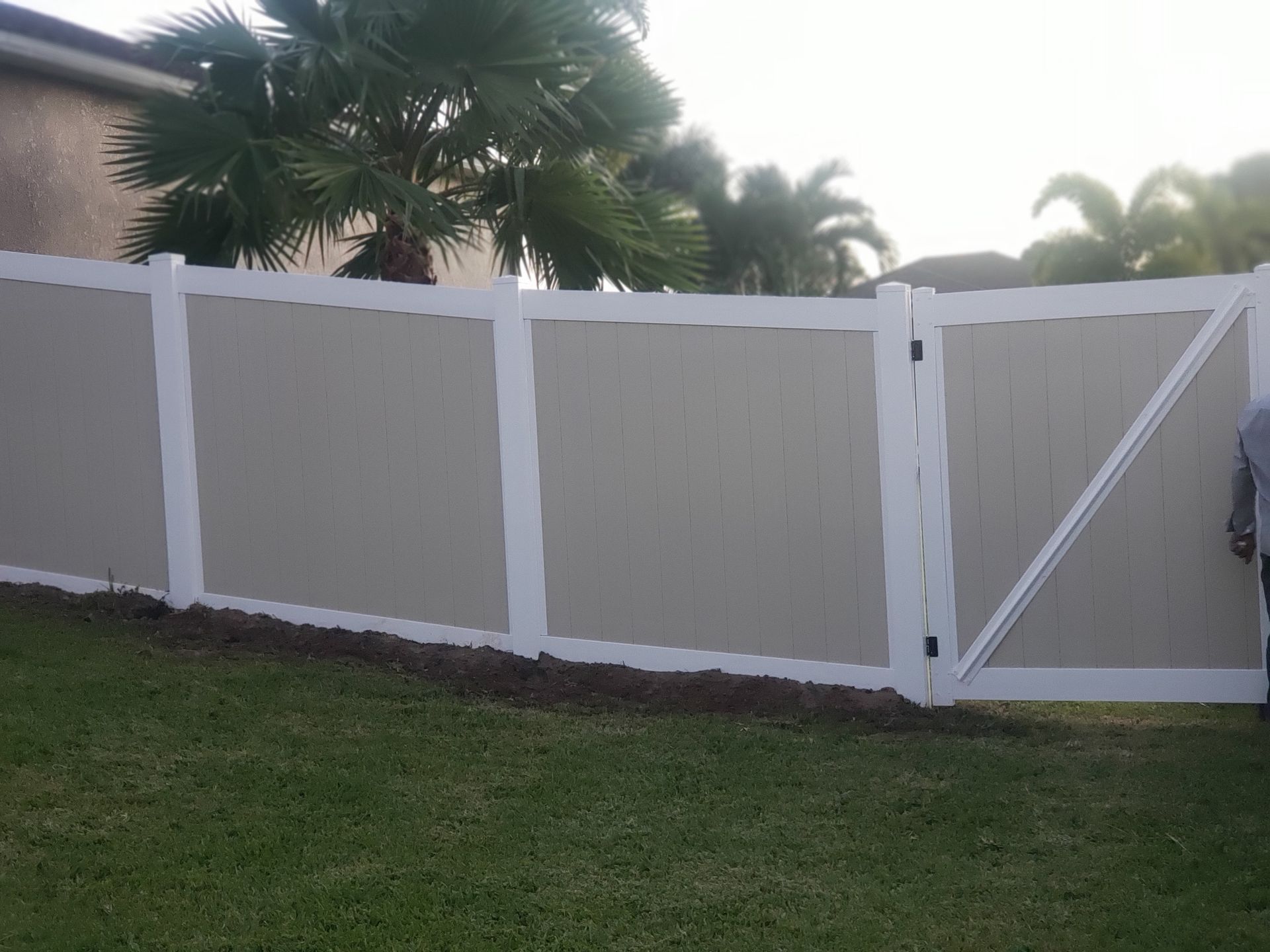 A white fence with a gate in the backyard of a house.