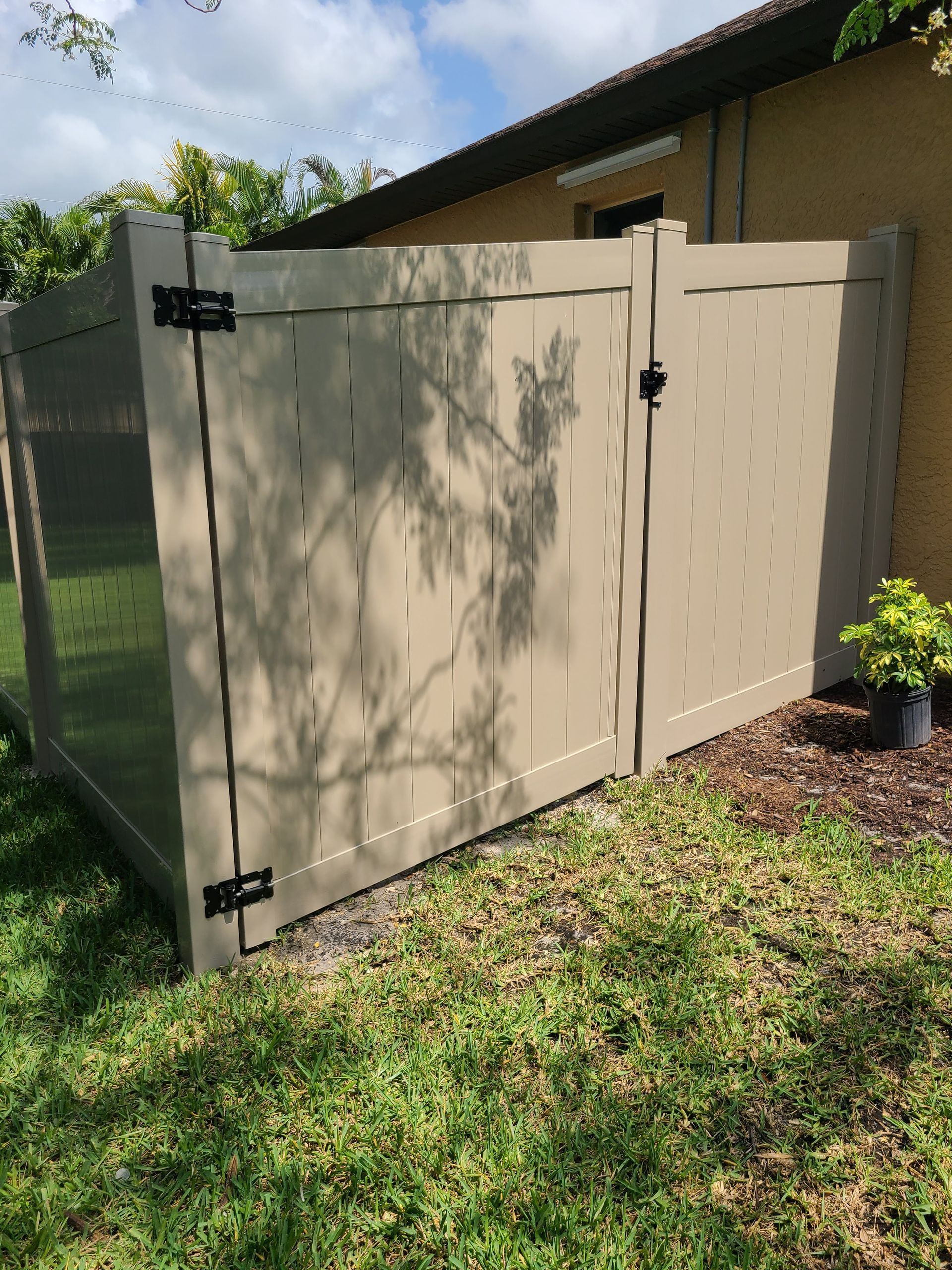A tan fence with a gate is sitting in the grass in front of a house.