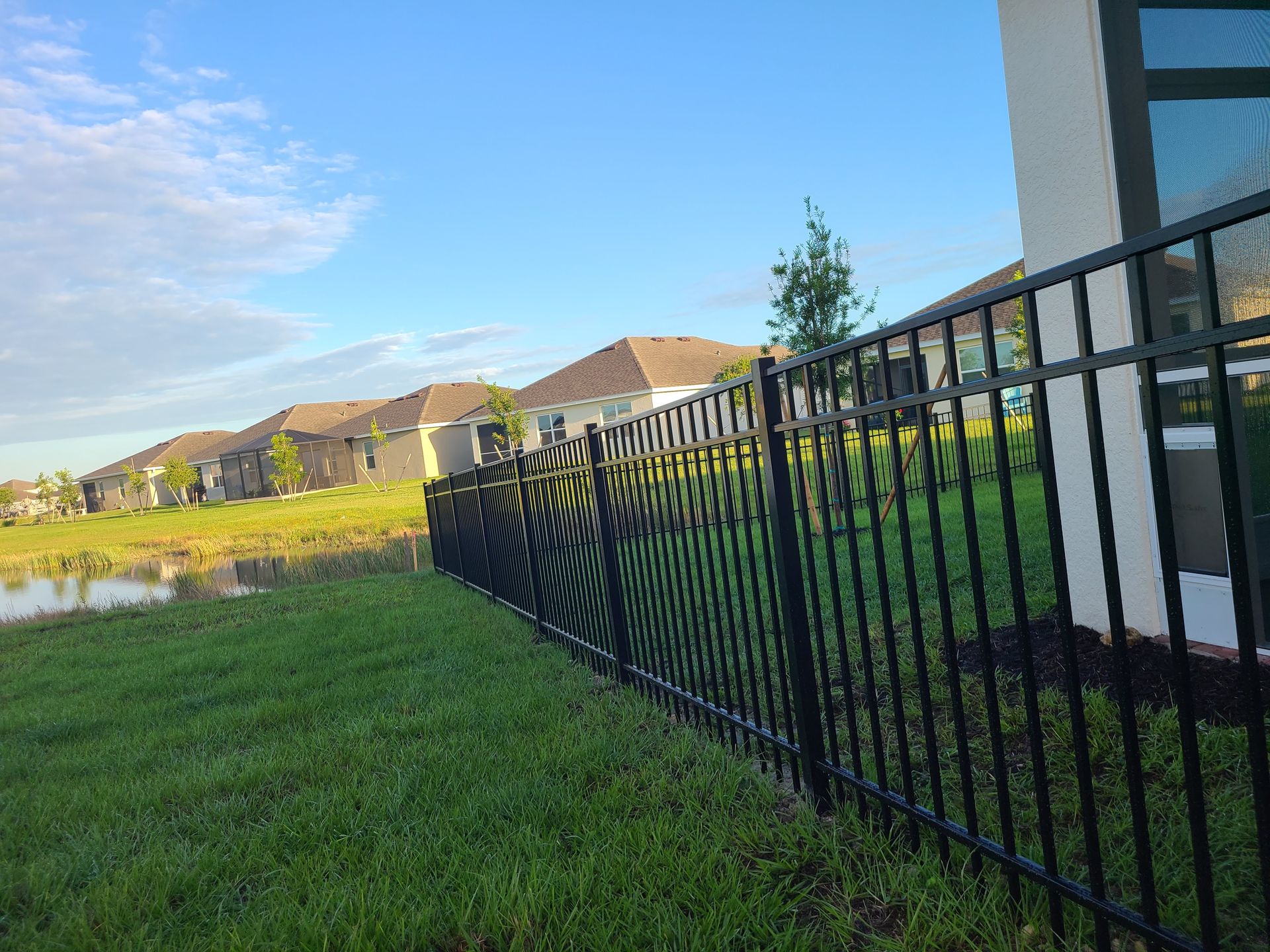 A black fence surrounds a lush green field in front of a house.