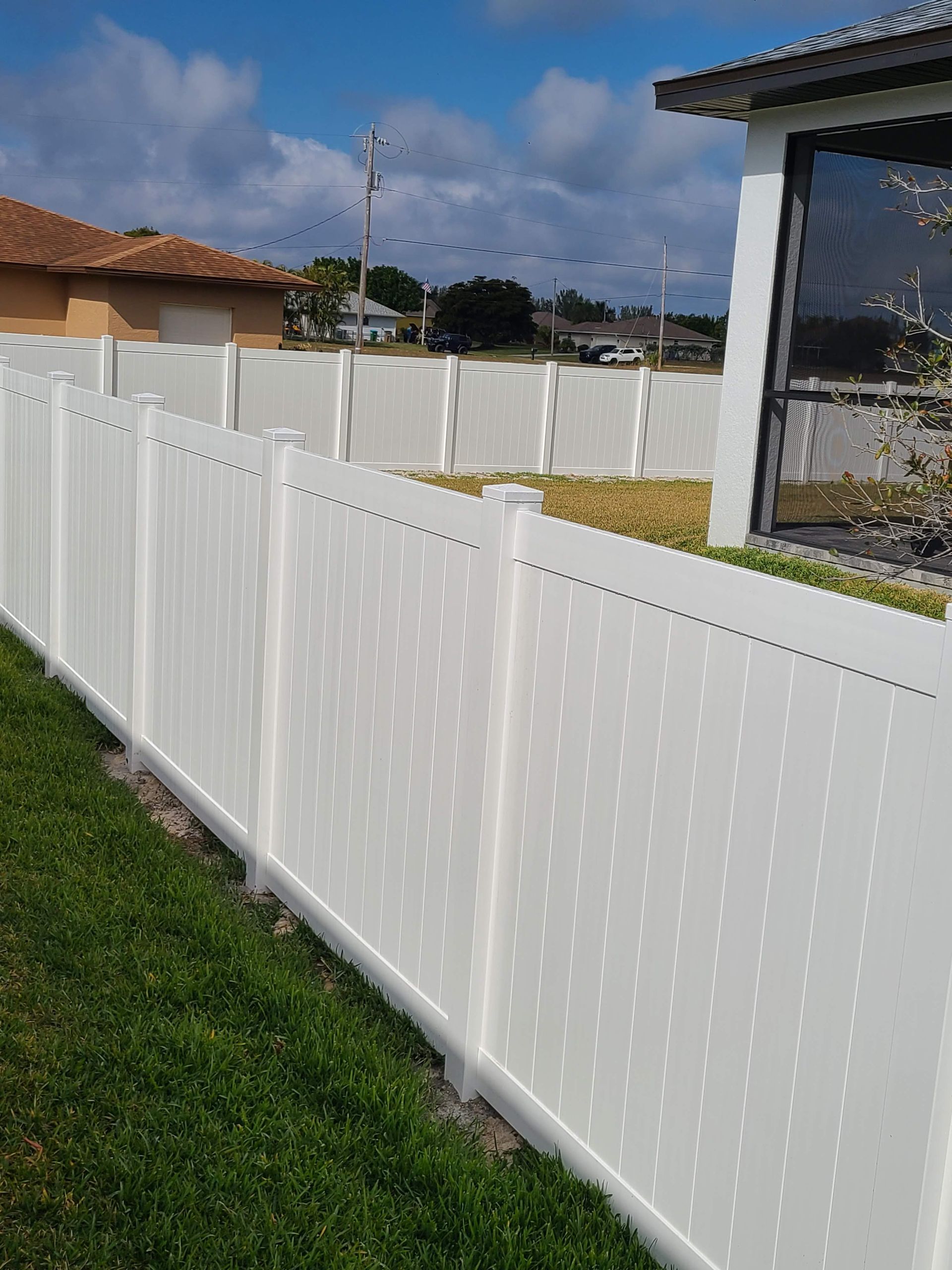 A white fence surrounds a lush green yard in front of a house.