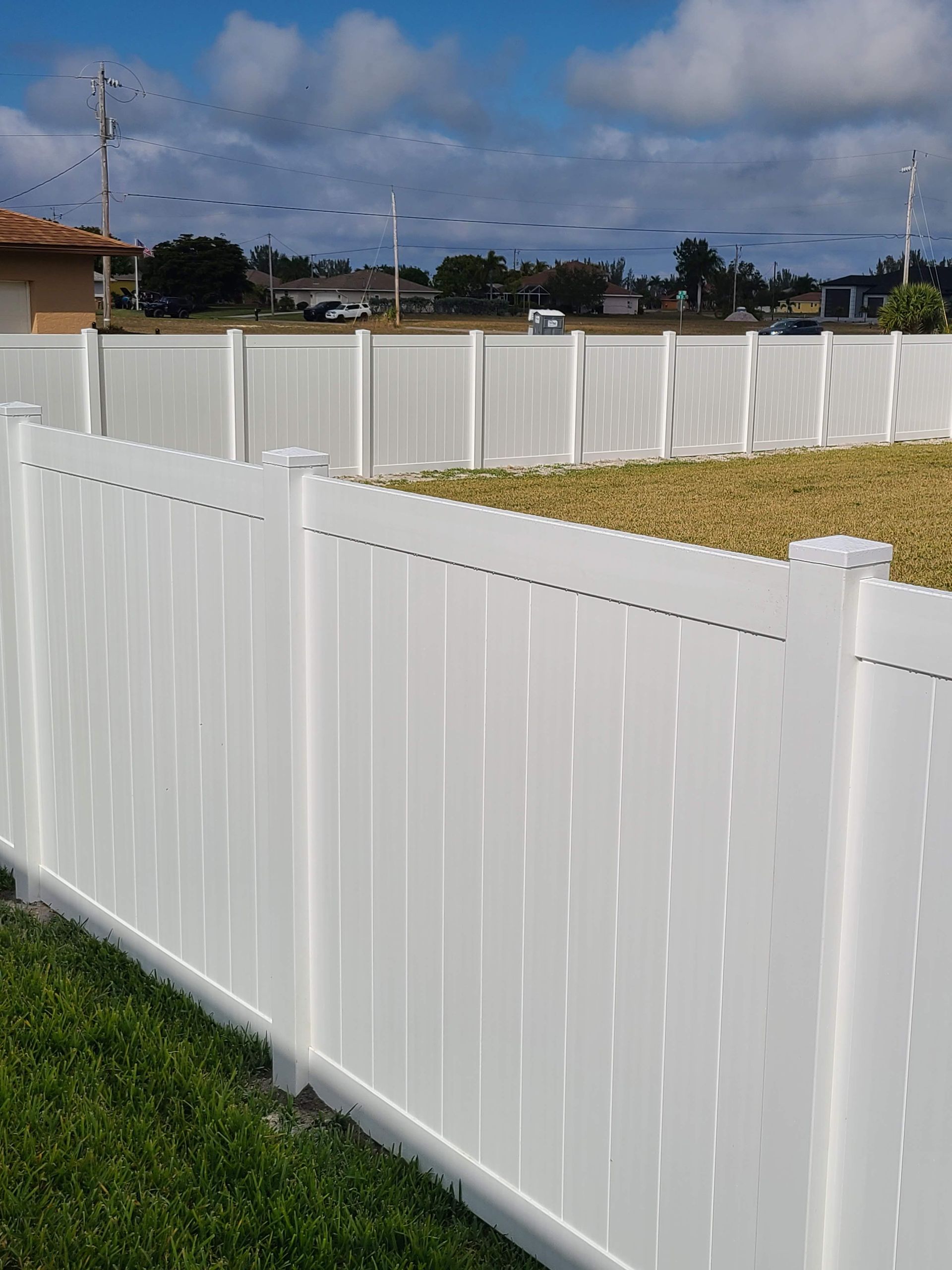A white vinyl fence is sitting on top of a lush green lawn.