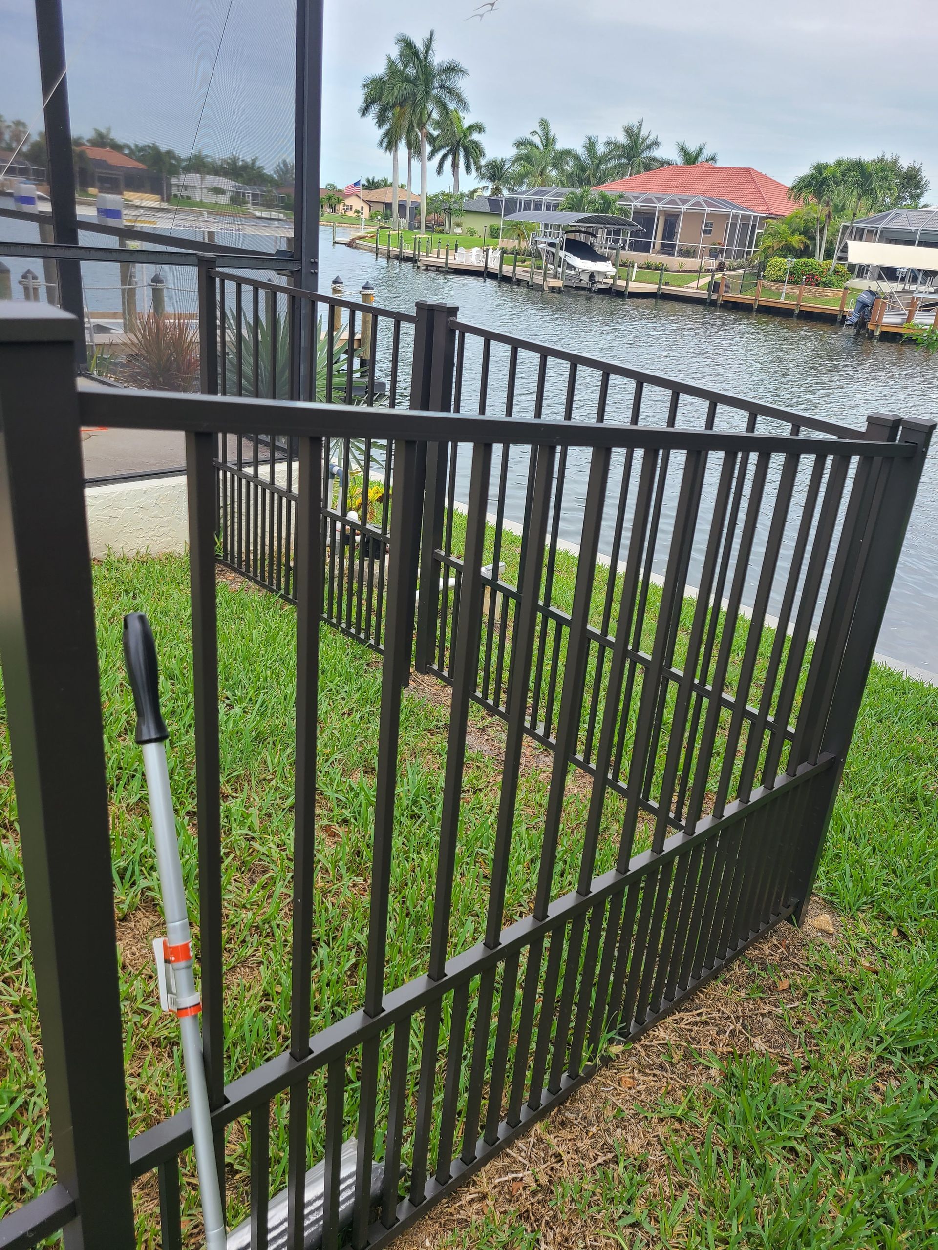 A wrought iron fence is sitting in the grass next to a body of water.
