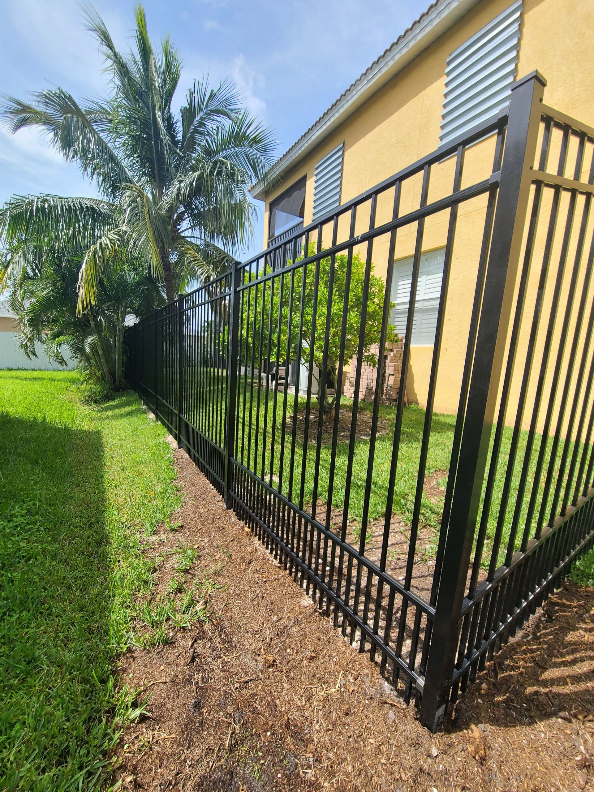 A black metal fence surrounds a lush green yard in front of a house.