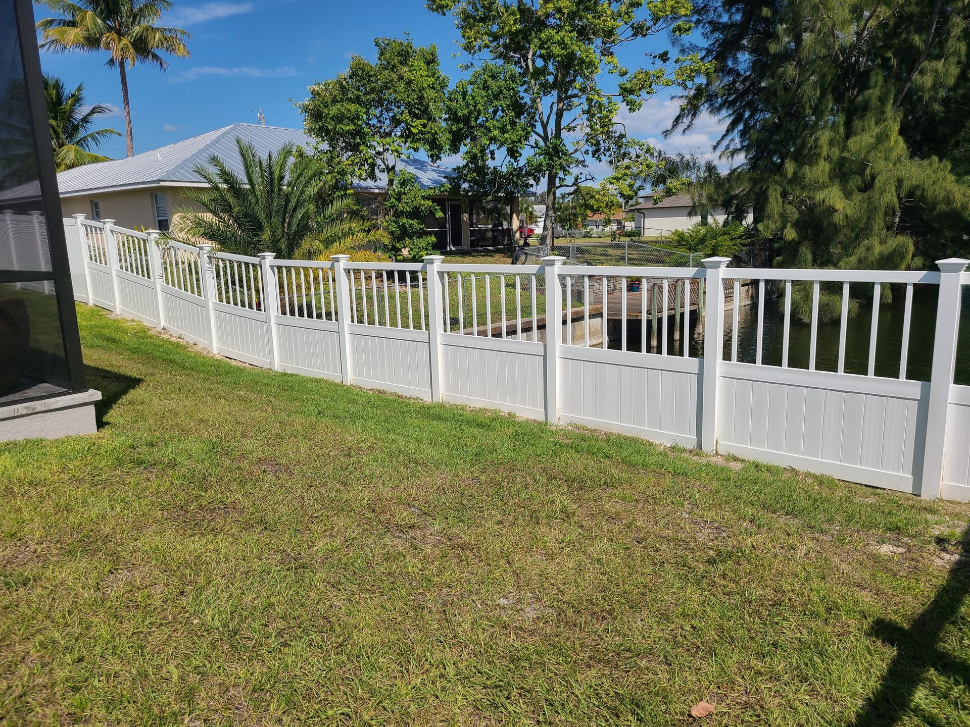 A white fence surrounds a lush green yard in front of a house.