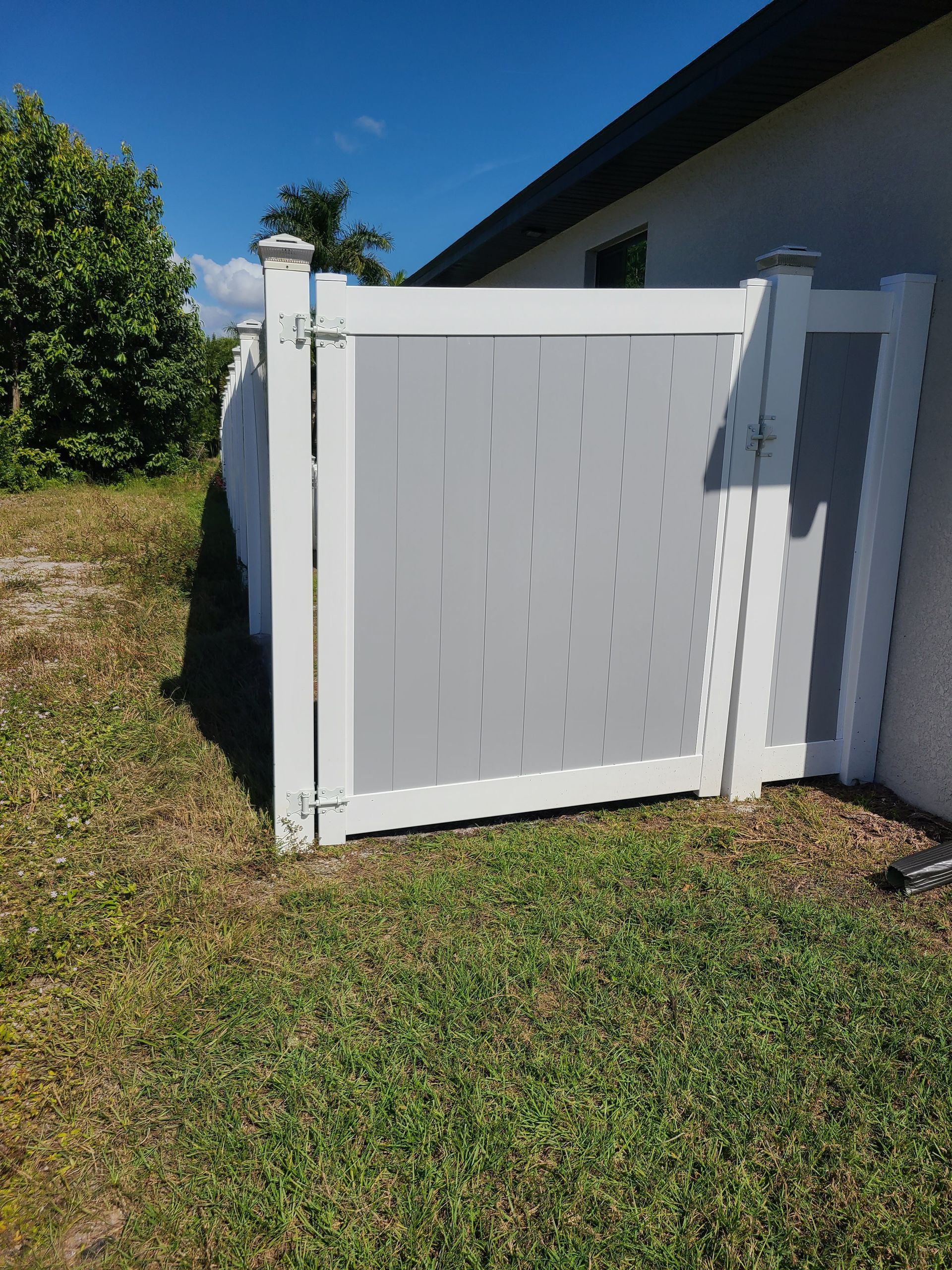 A white fence with a gate is sitting in the grass in front of a house.