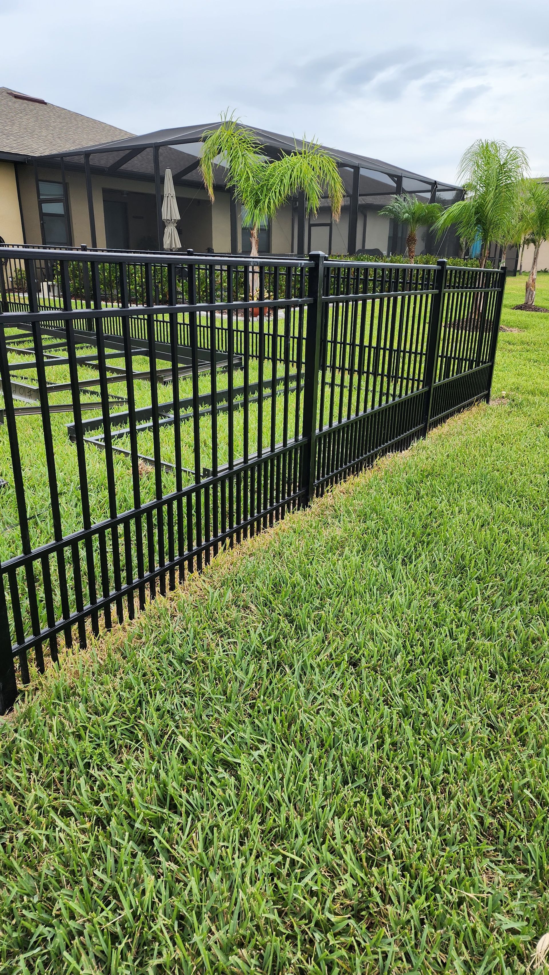A black fence surrounds a lush green lawn in front of a house.
