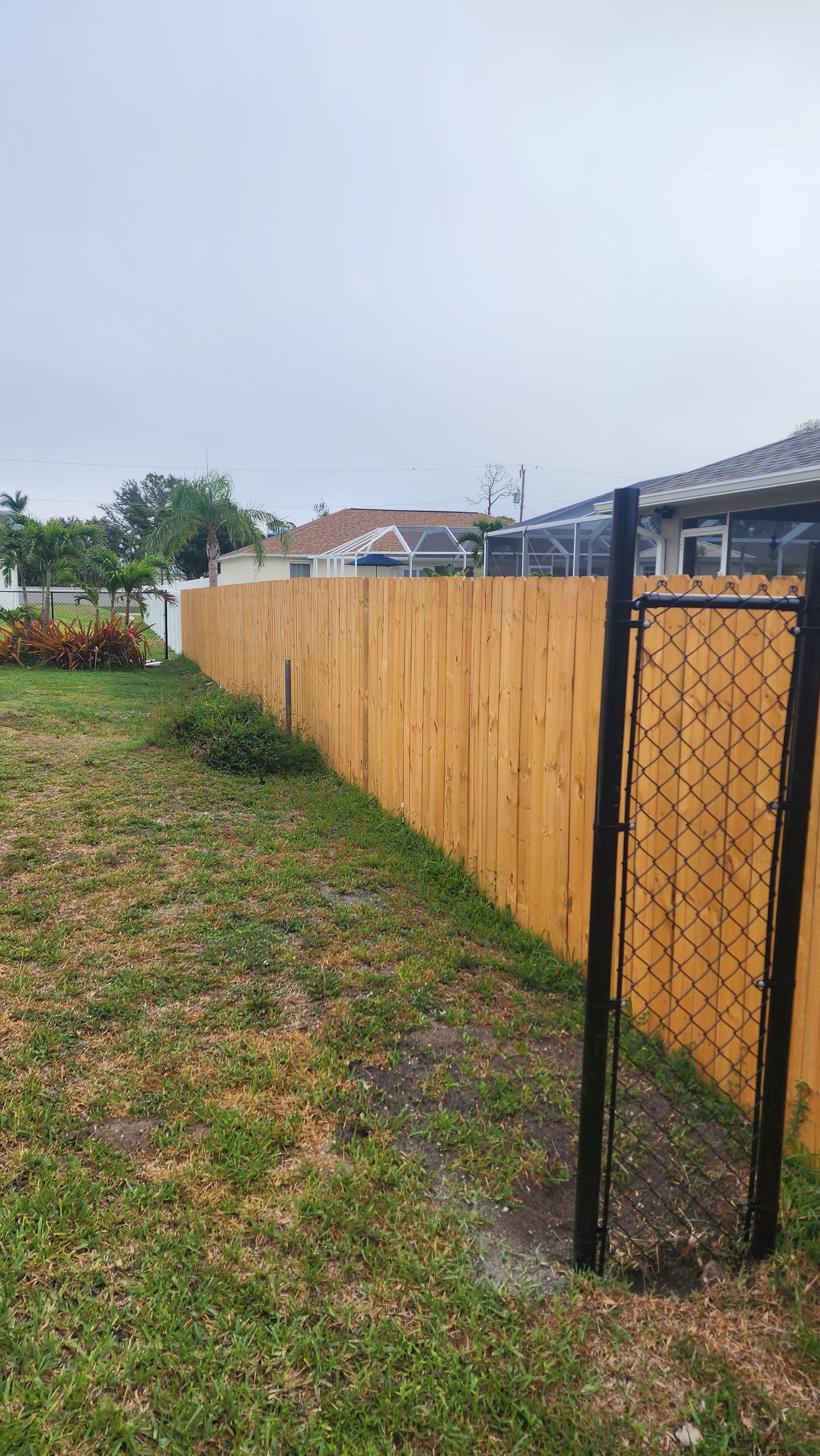 A wooden fence with a chain link fence in the backyard of a house.