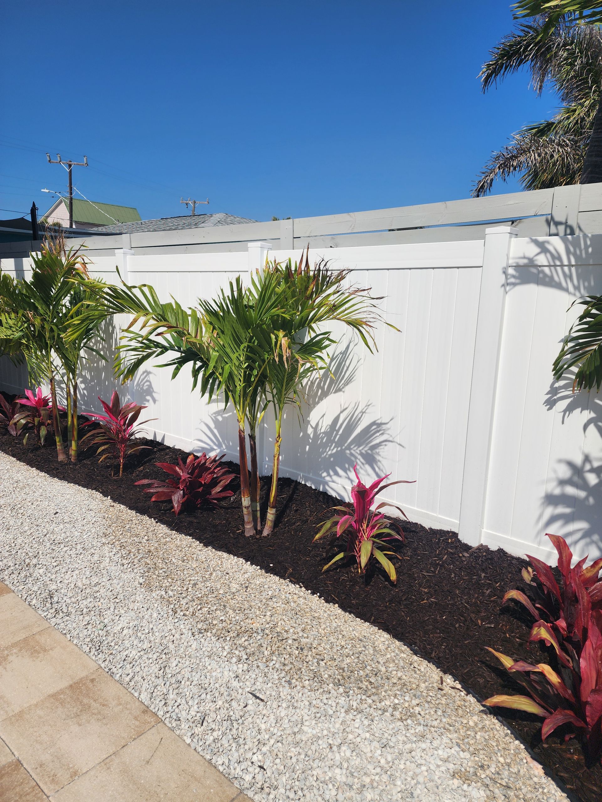 A white fence surrounds a garden with plants and gravel.