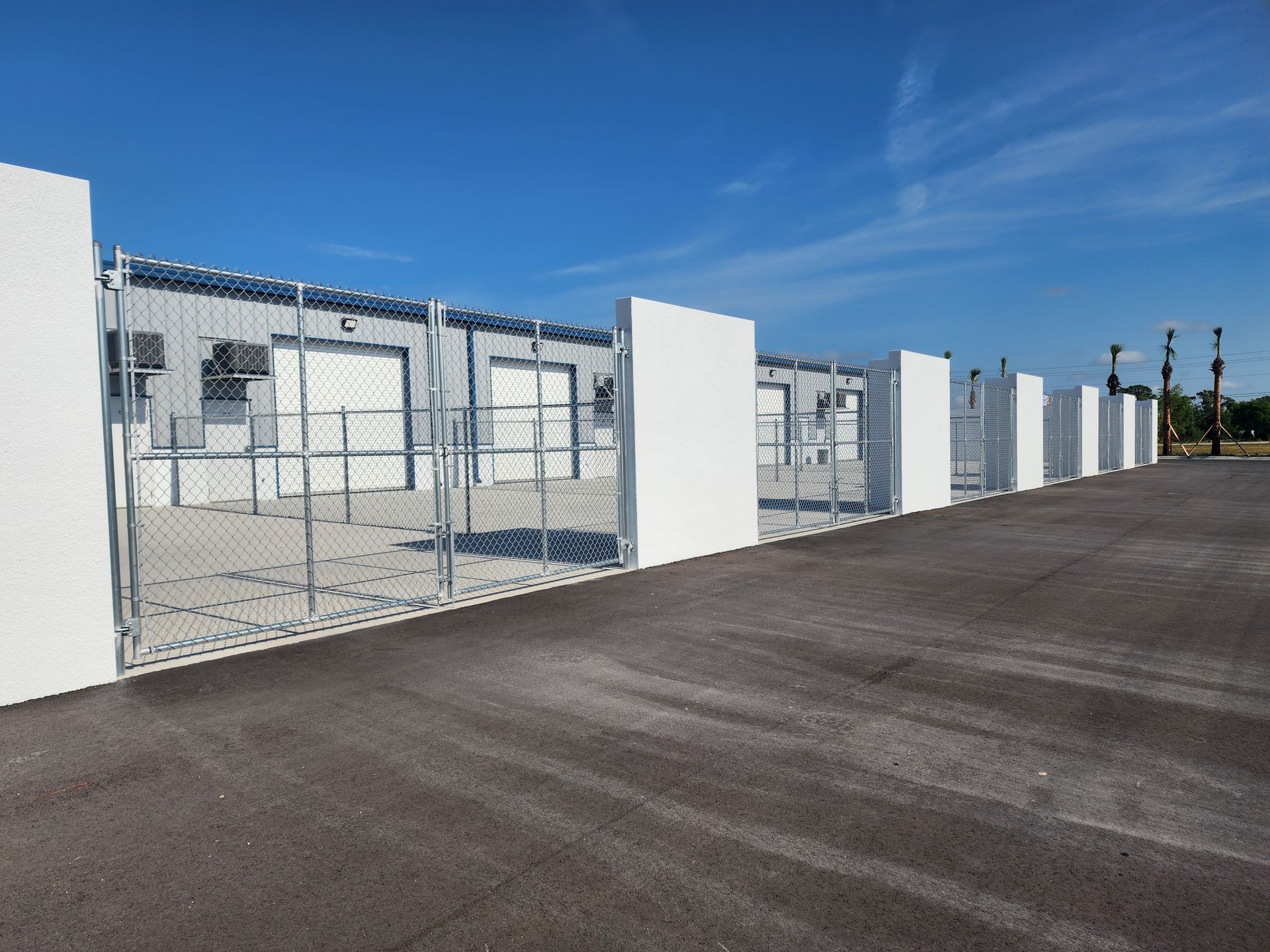 A chain link fence surrounds a parking lot with a building in the background.