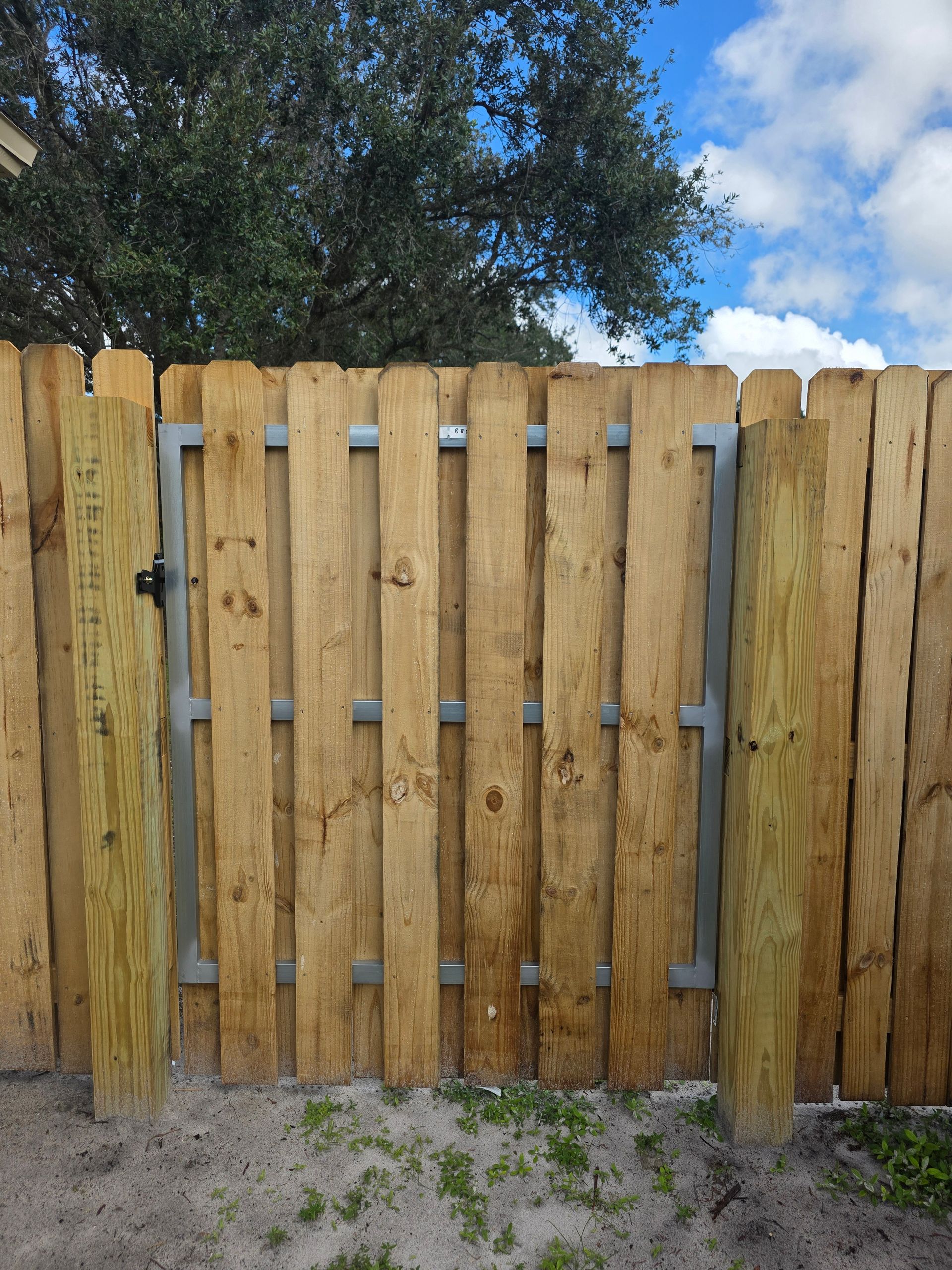 Wooden gate in a fence, with metal supports. Green grass and blue sky are in the background.