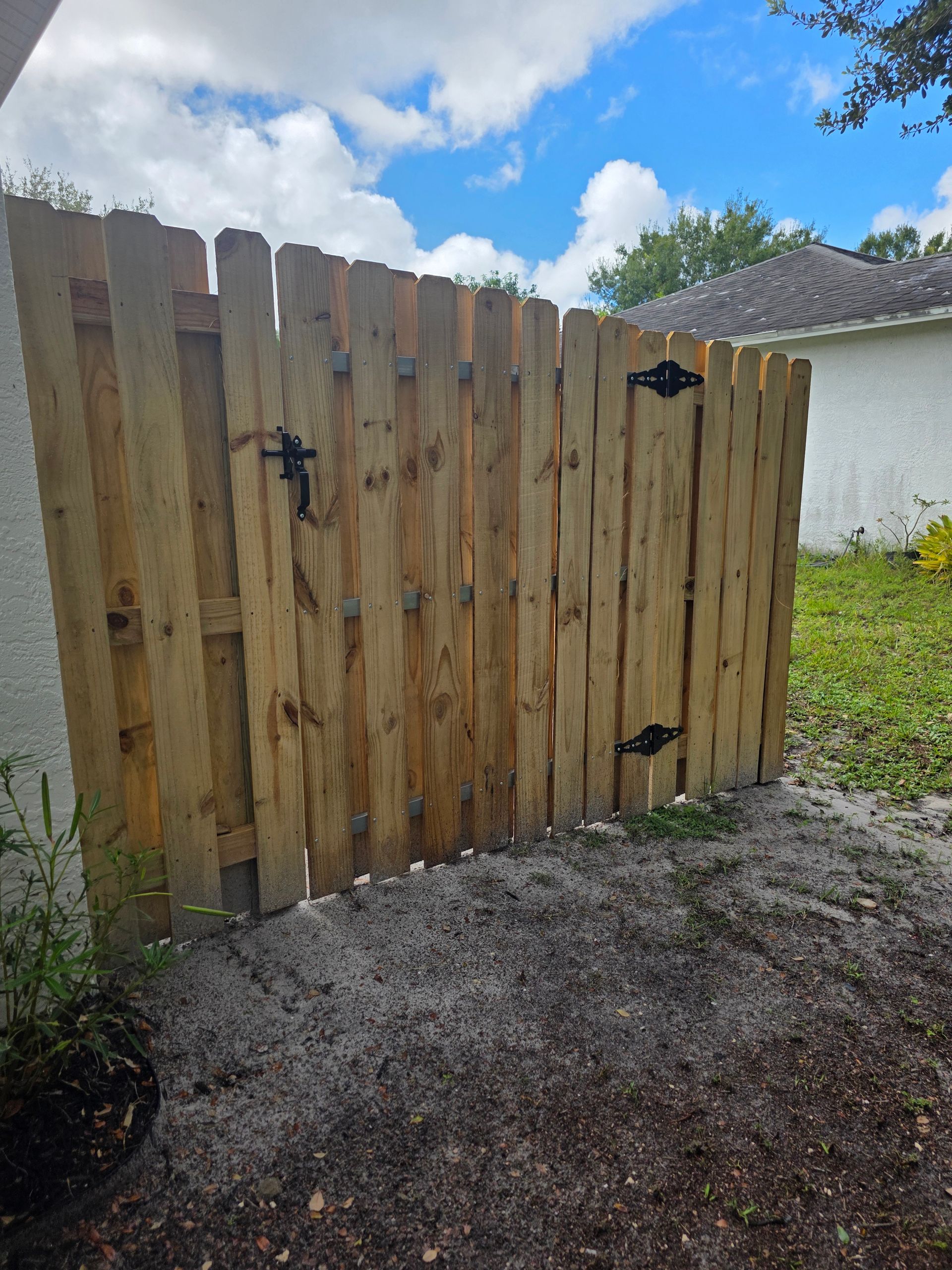 Wooden fence and gate, tan with black hardware. Outdoor setting, overcast sky.