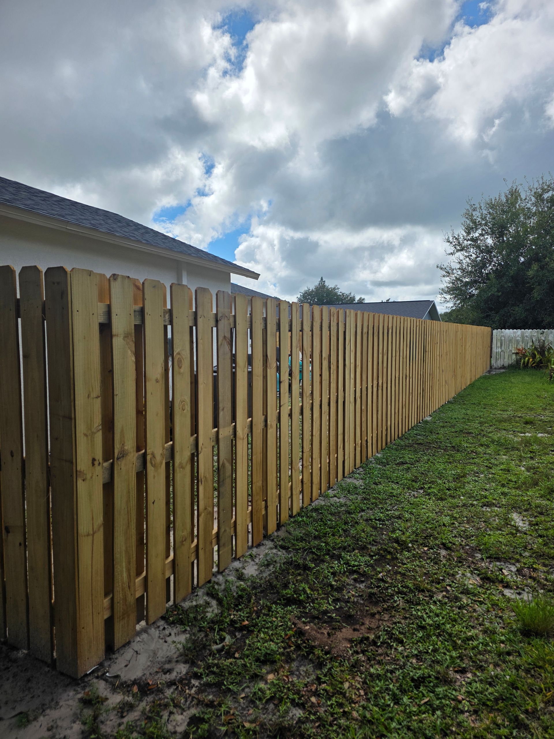 Wooden fence in a backyard under a cloudy sky.