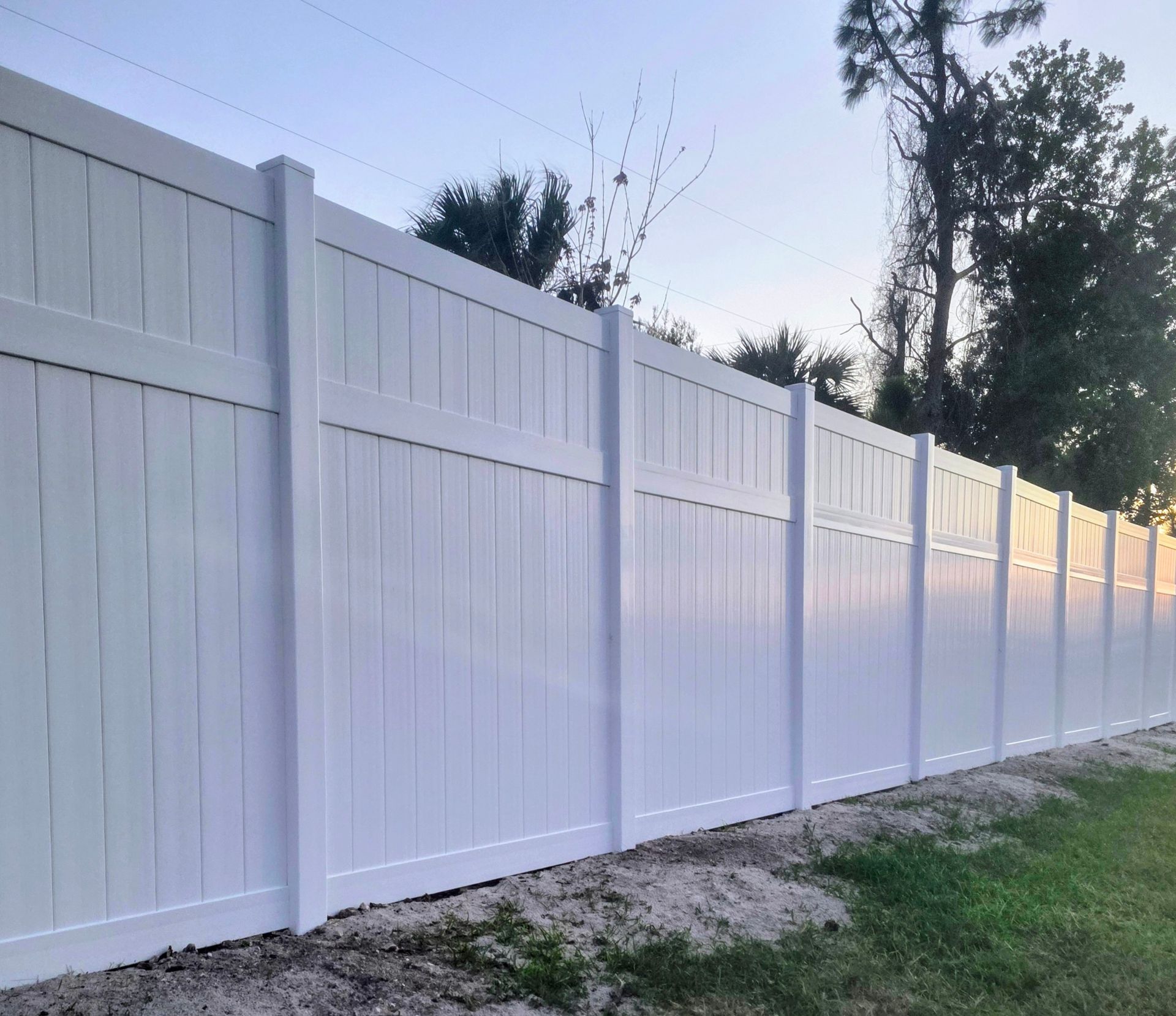 White vinyl privacy fence along a grassy yard at dusk.