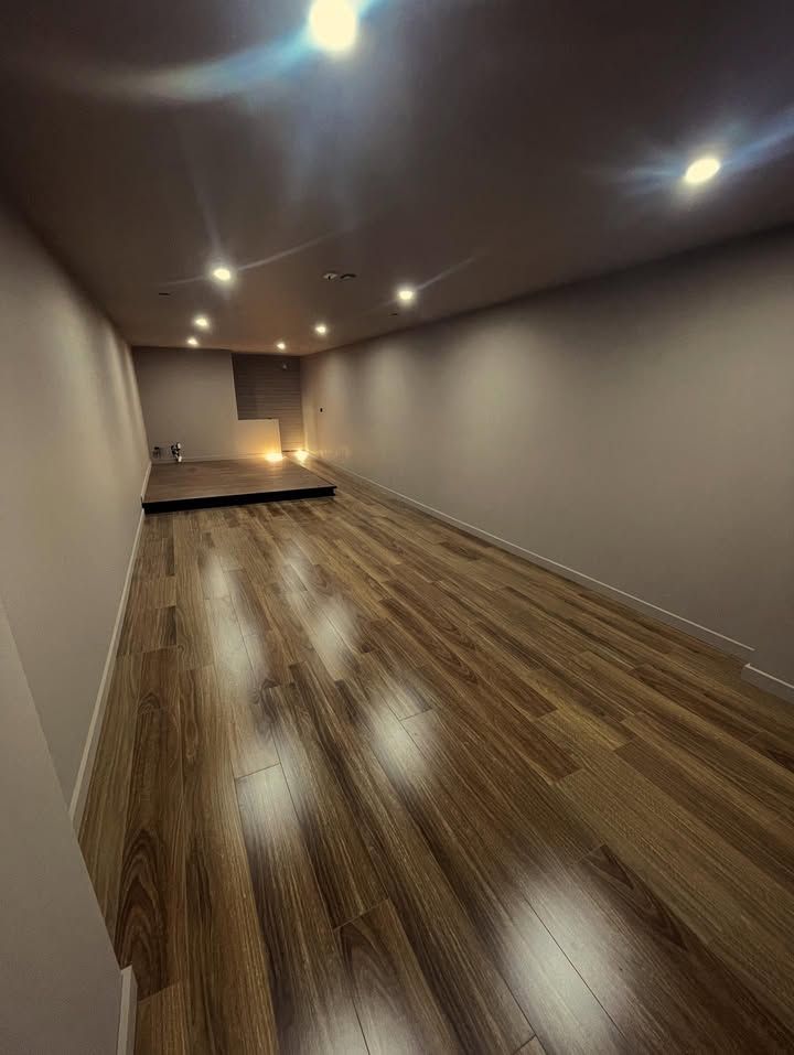 Empty room with wood floors, recessed ceiling lights, and a small raised platform at the far end