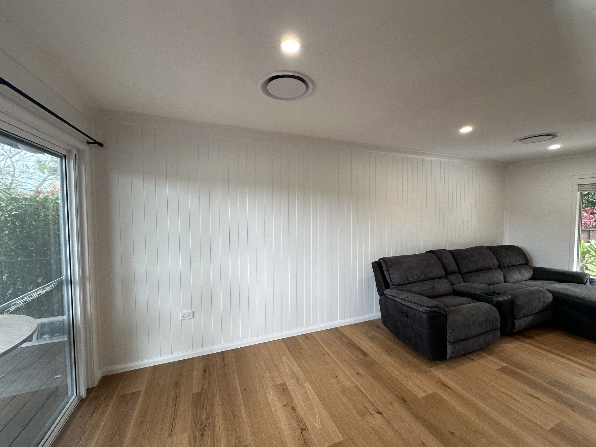 Bright living room with wood floors, white walls, sliding glass door, and a dark sectional sofa.