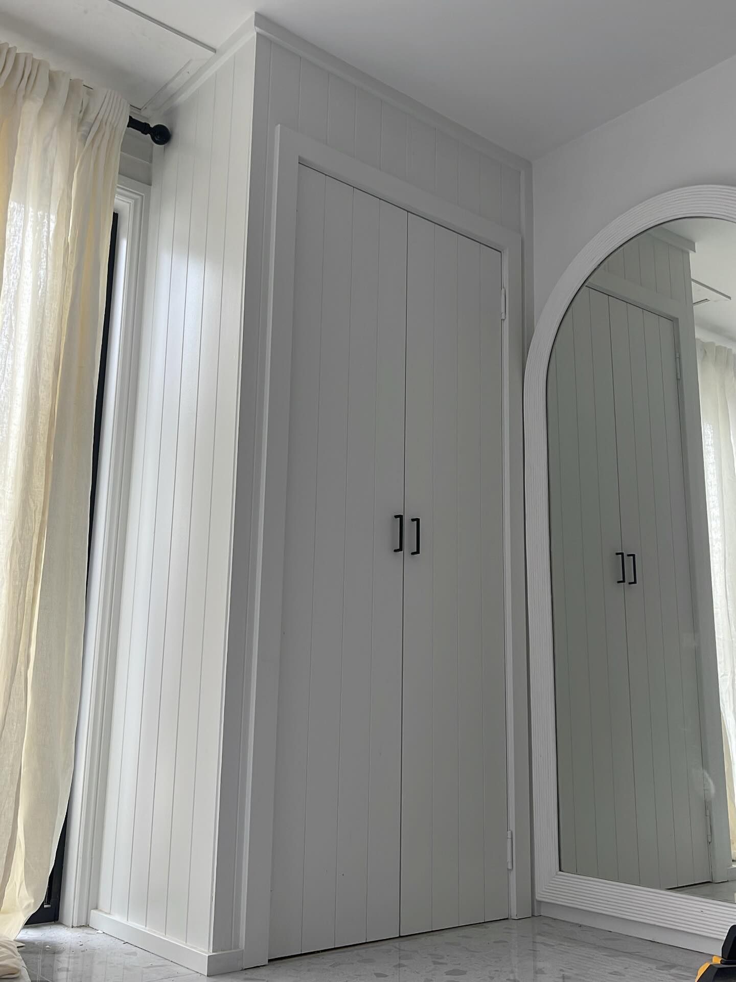 White closet doors beside a tall arched mirror in a bright, minimalist room.