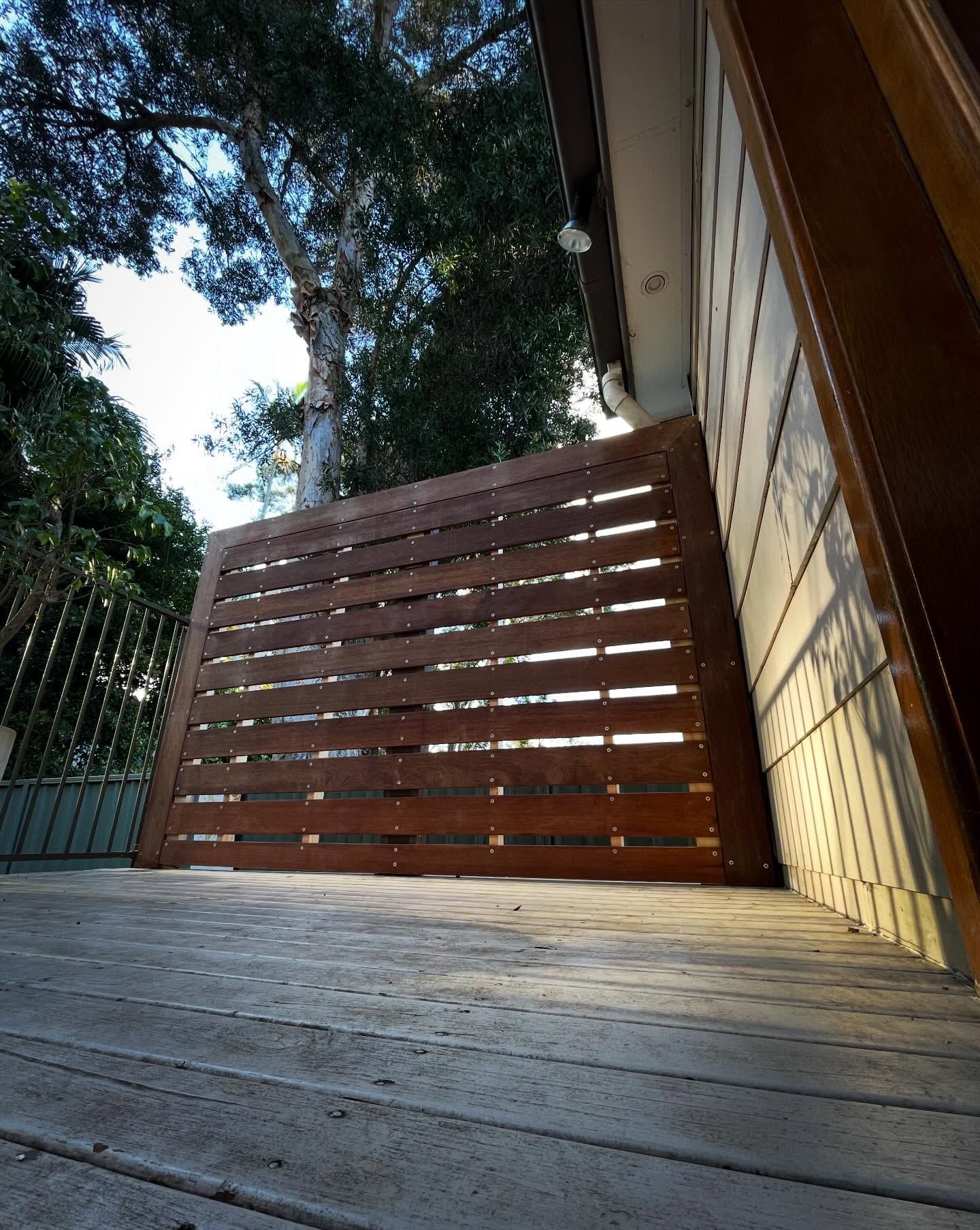 Wooden deck with slatted privacy screen beside a house, framed by trees and sky.