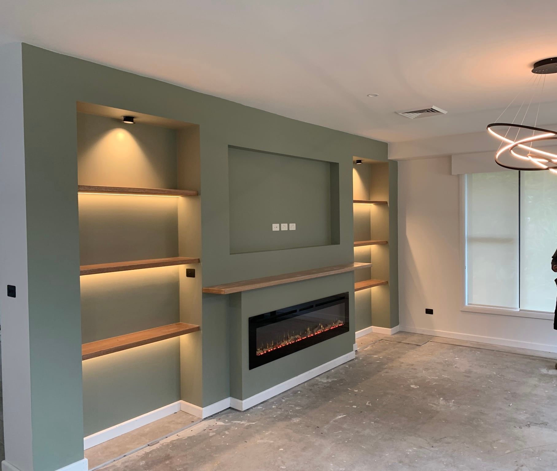 Modern empty living room with built-in shelving, wall fireplace, gray walls, and large windows