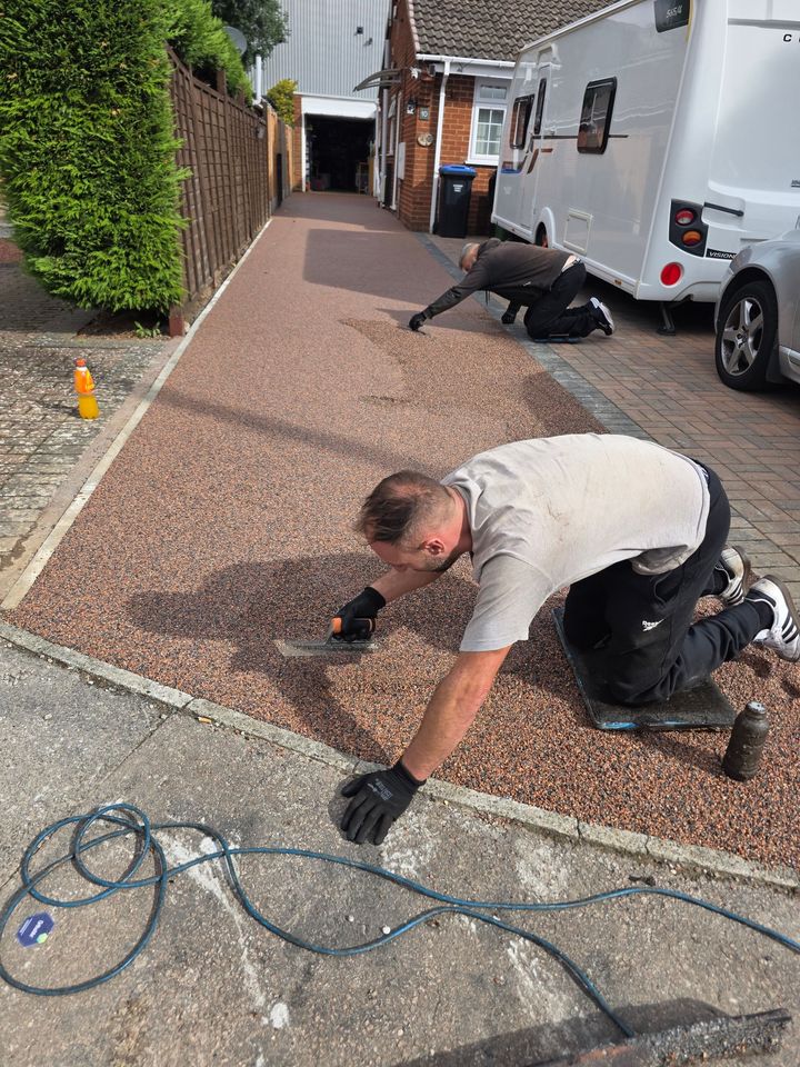 Worker kneeling on a pebble driveway handling cables beside a white van and driveway wall