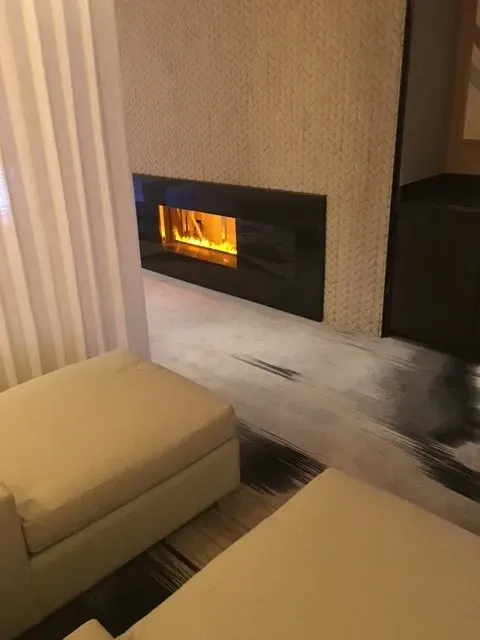 Modern living room with a lit wall-mounted fireplace, beige ottomans, and patterned rug