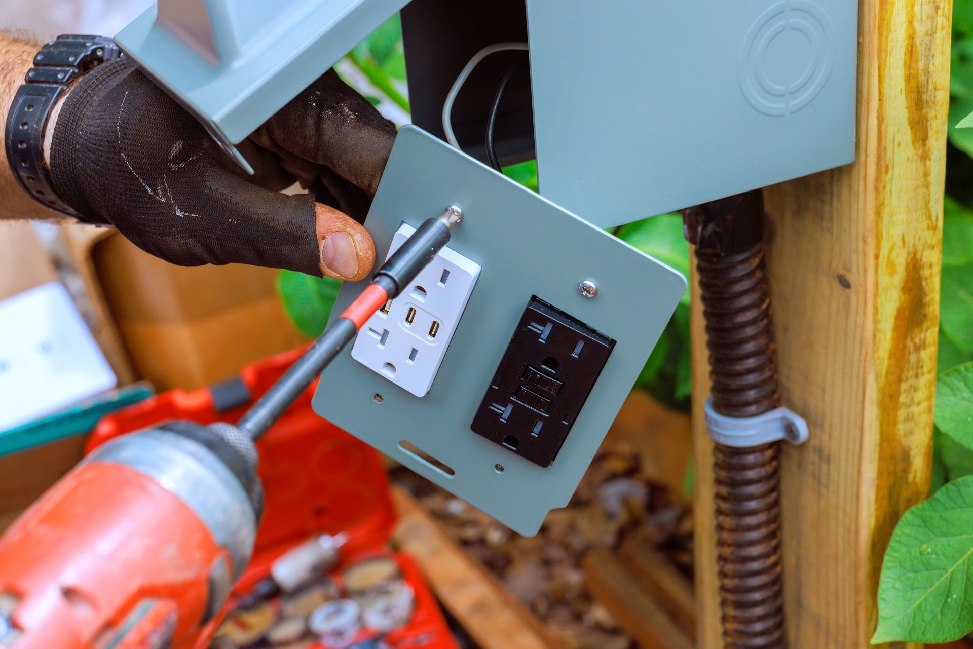 Gloved hands using a power drill to install a new outdoor electrical outlet plate with USB ports.