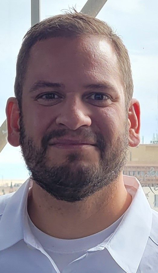 A man with a beard and a white shirt is smiling for the camera.