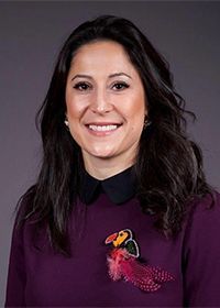 A woman wearing a purple sweater with a toucan on it is smiling for the camera.