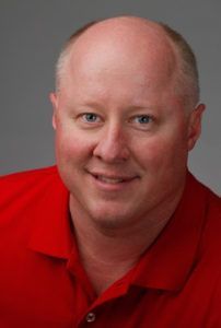 A bald man wearing a red shirt is smiling for the camera.