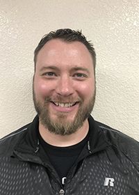 A man with a beard is smiling and wearing a black jacket.