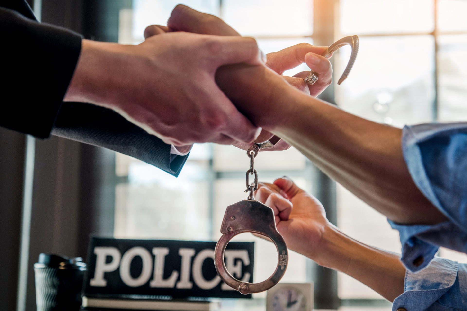 Handcuffed suspect being arrested by police officer near a POLICE desk sign