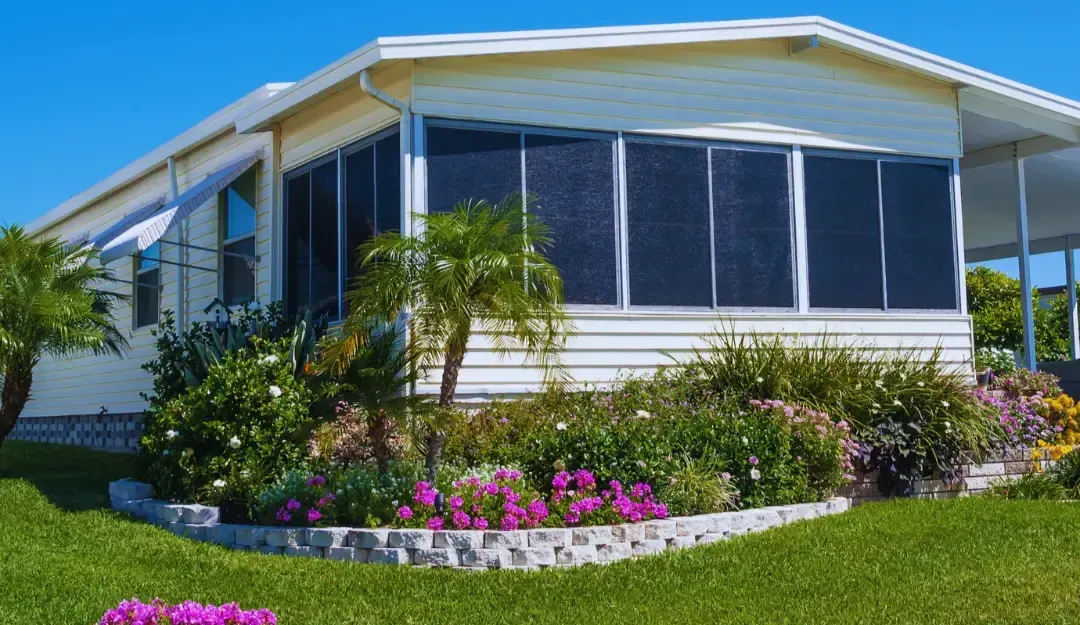 A mobile home with a screened in porch and flowers in front of it.