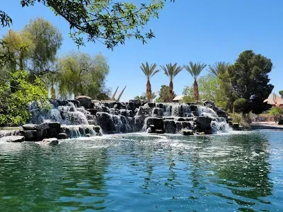 There is a waterfall in the middle of a pond surrounded by palm trees.