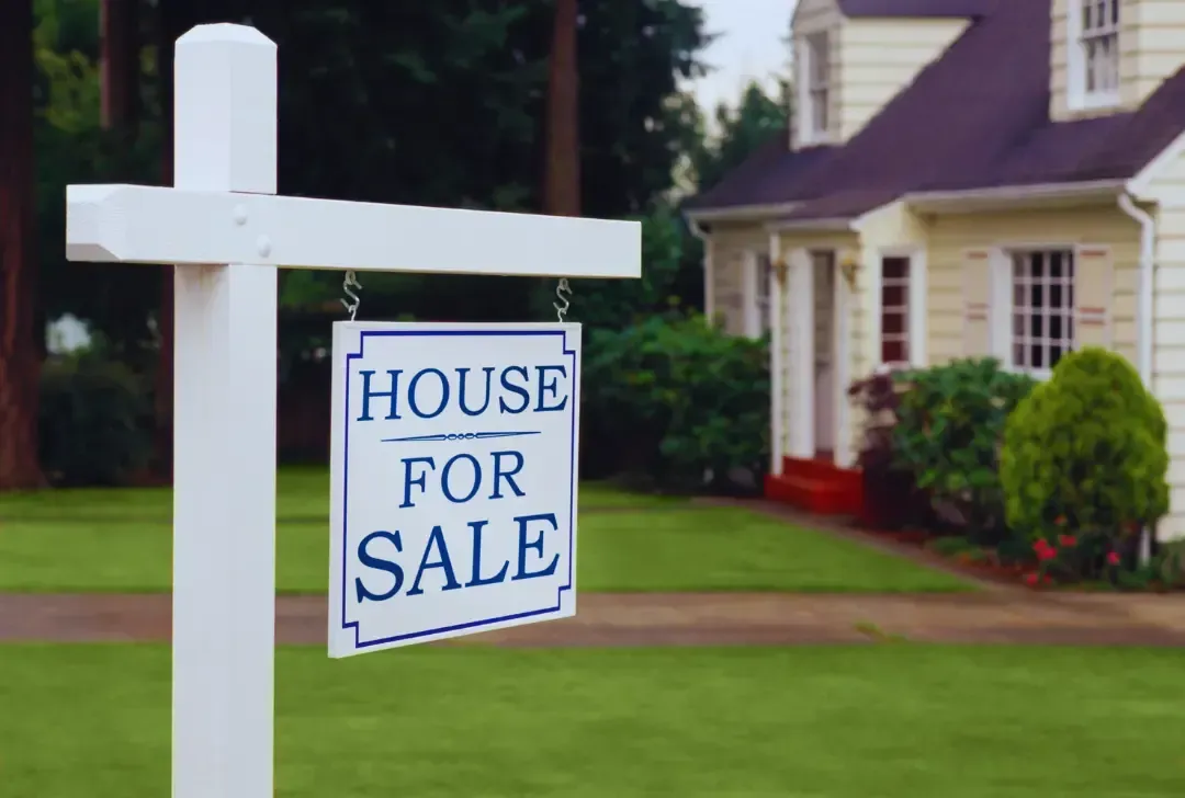 A house for sale sign is hanging in front of a house.