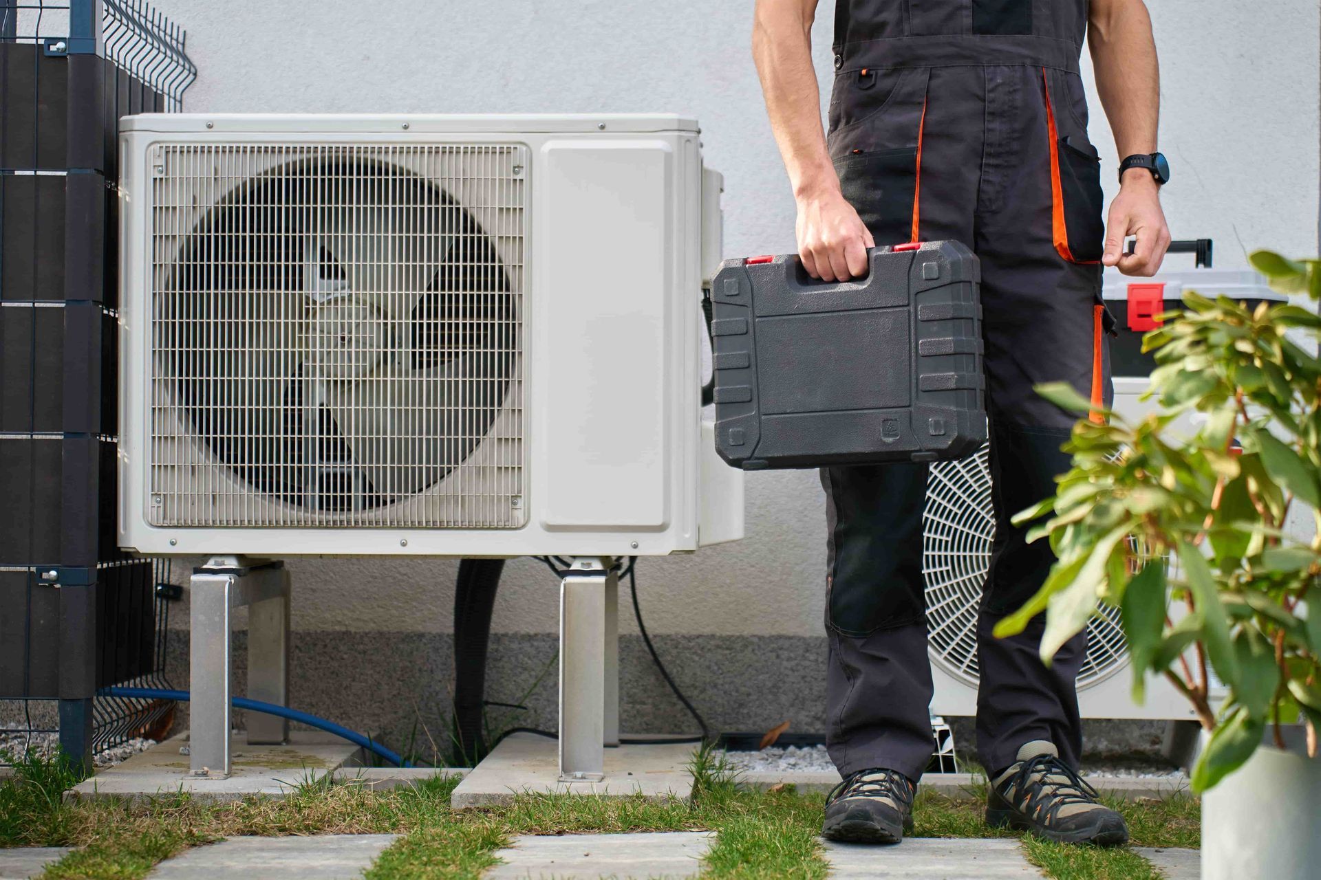 Technician carrying a toolbox beside an outdoor air conditioner unit
