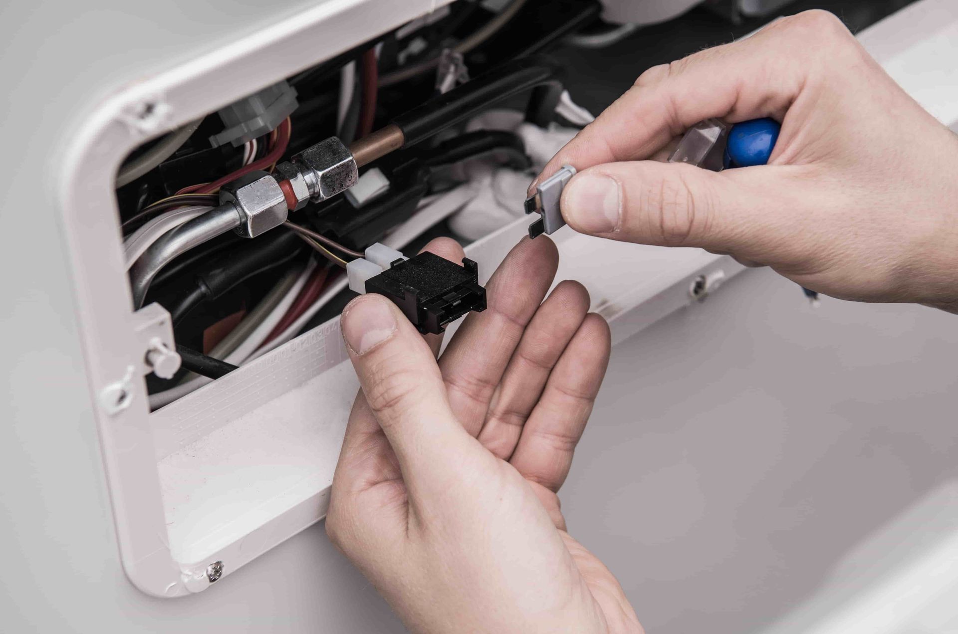 Hands using pliers to repair wiring inside an open white appliance panel