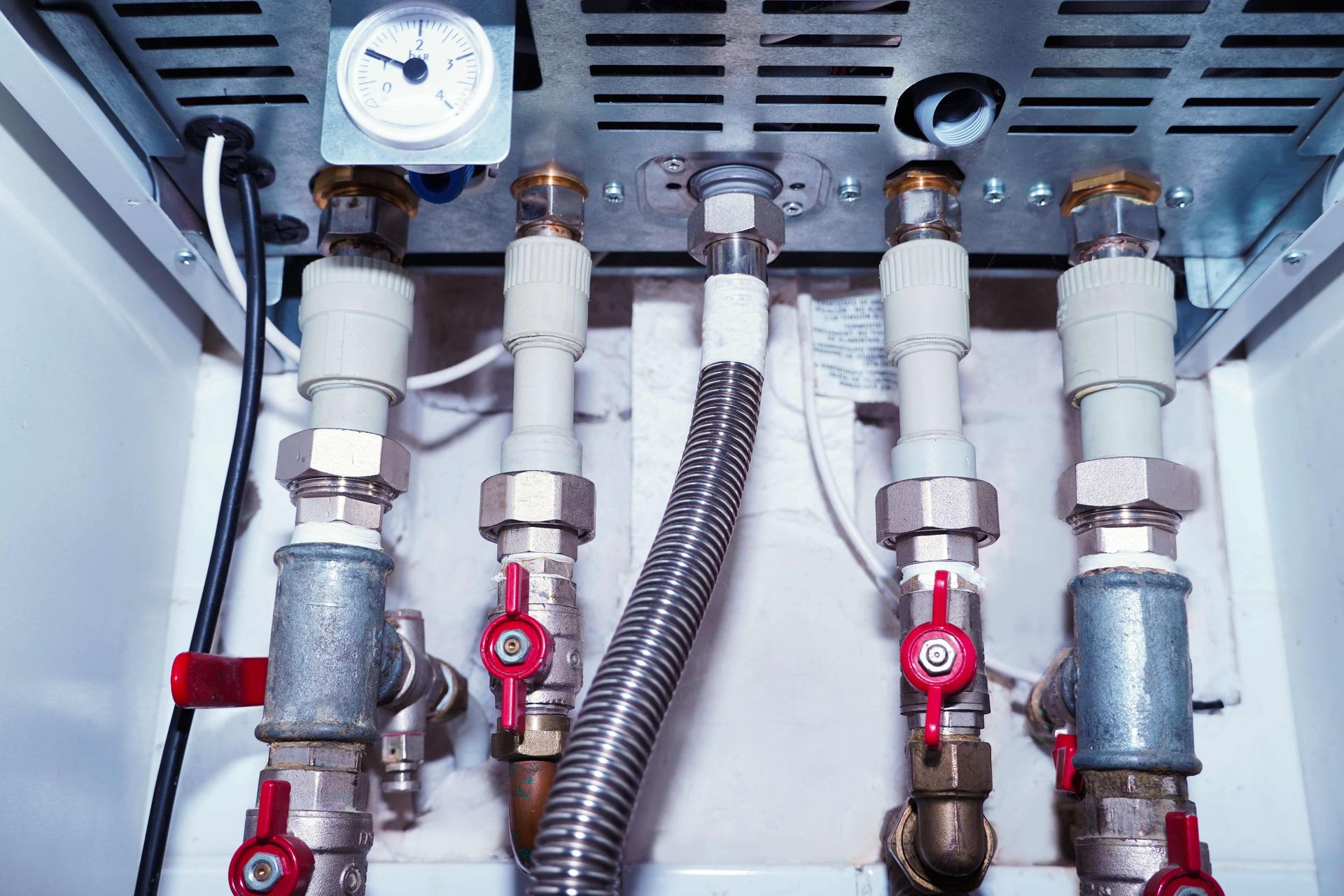Close-up of industrial pipes and valves with a pressure gauge inside a metal cabinet