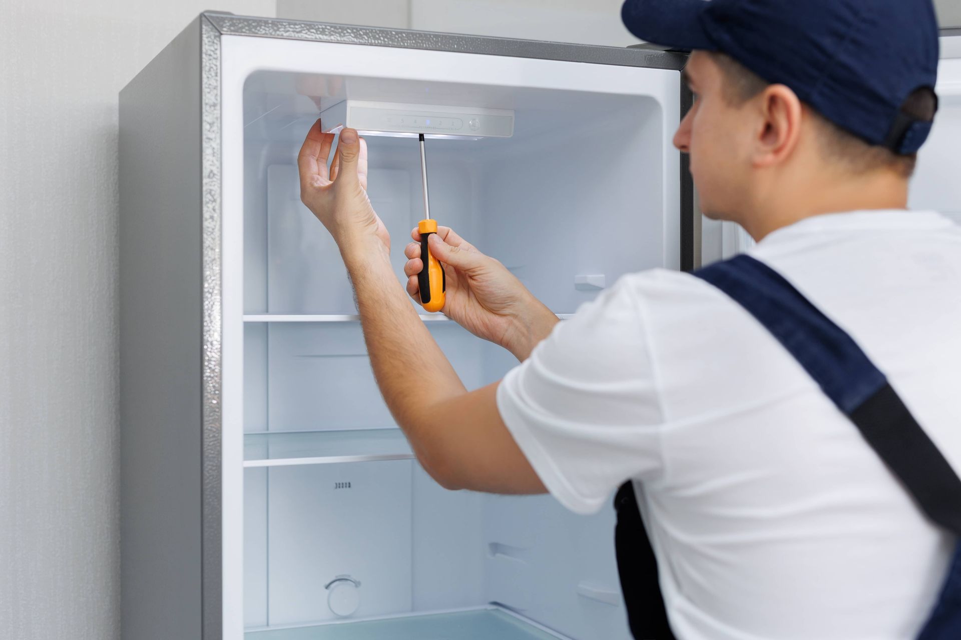Technician replacing a refrigerator light bulb inside an open fridge