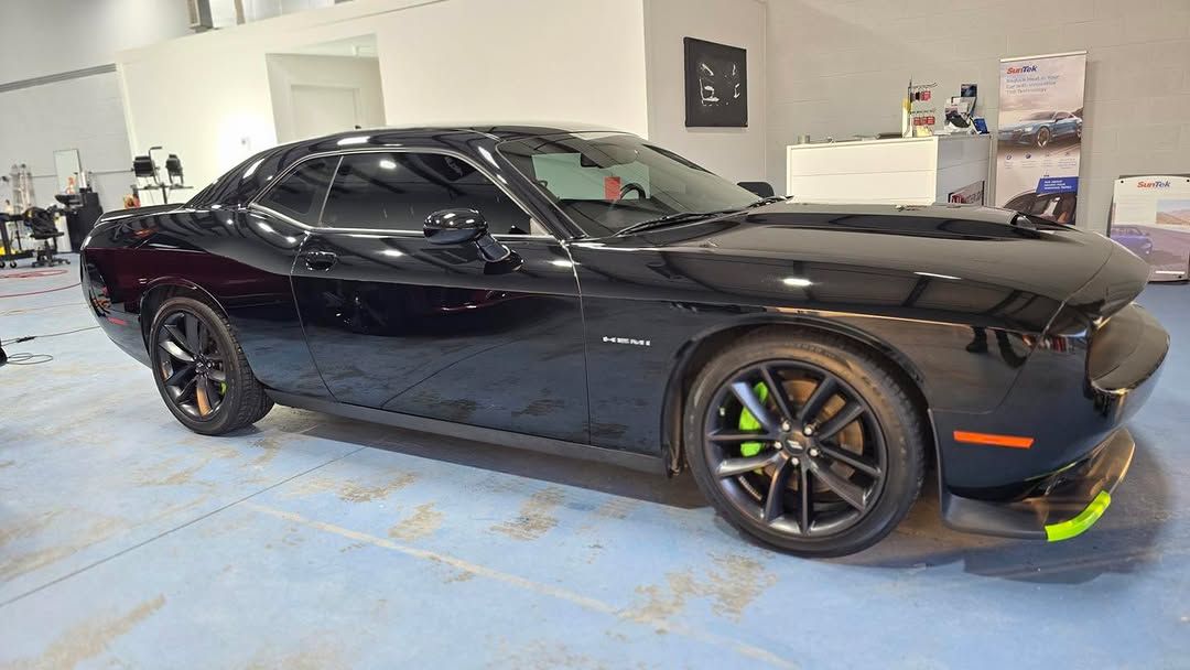 Black Dodge Challenger sports car with green brake calipers.