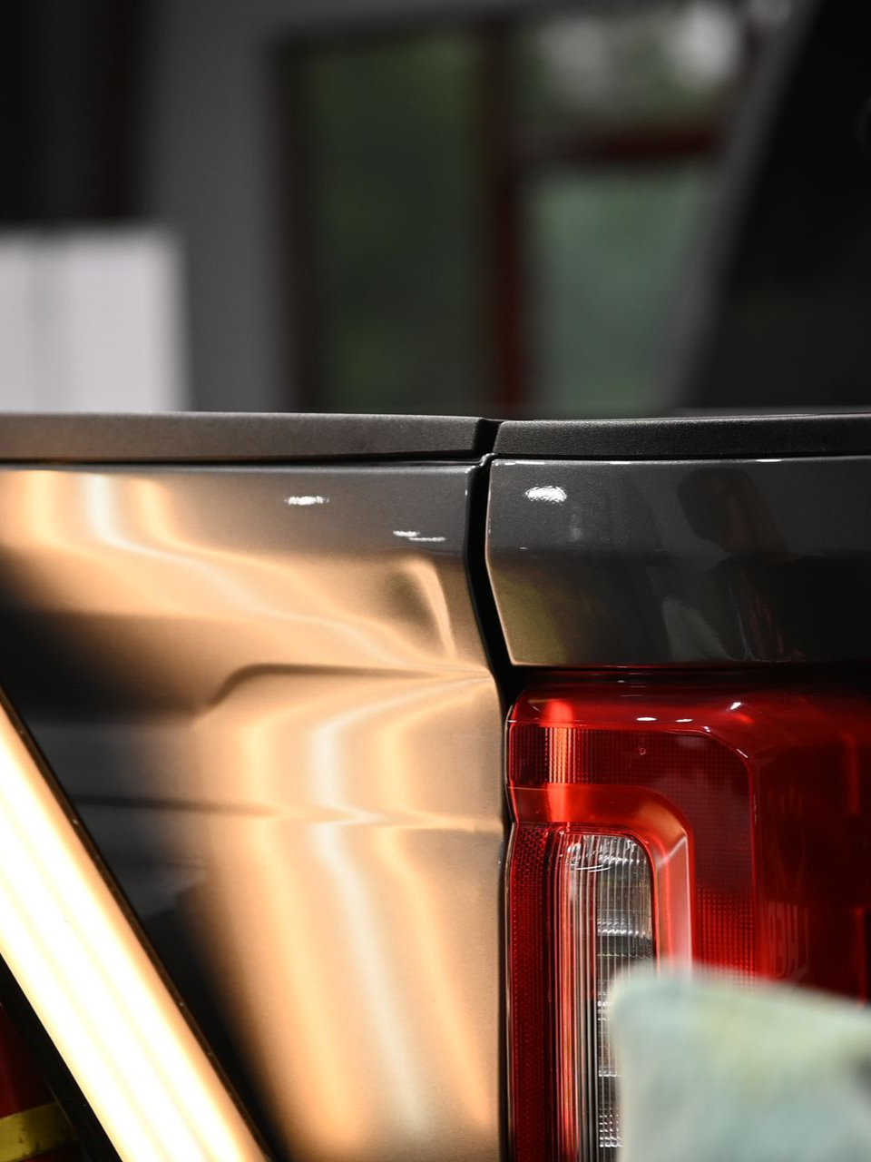 Two people applying film to the side of a black vehicle in a garage.