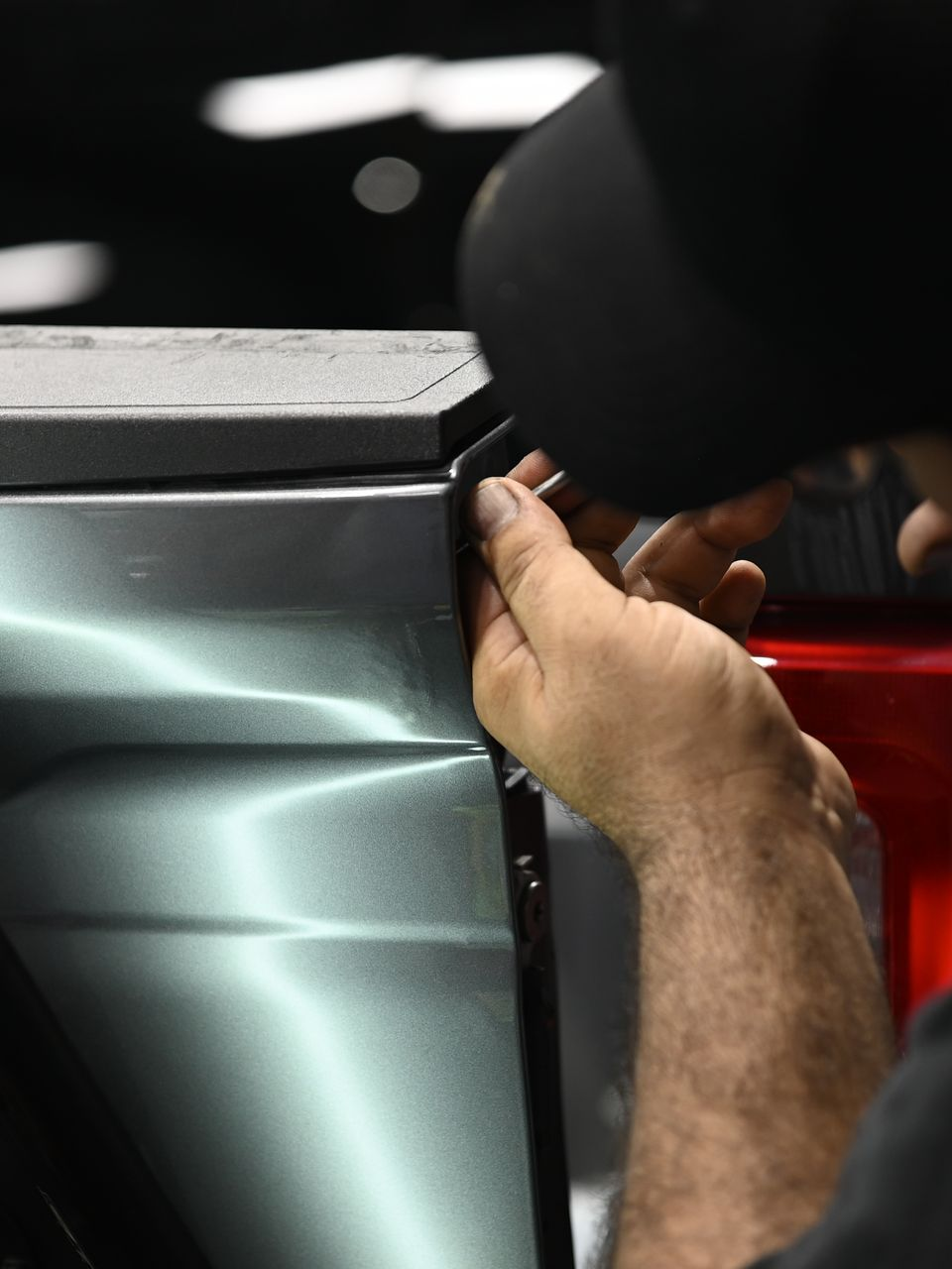 Hands repairing a red car hood in a garage or workshop.